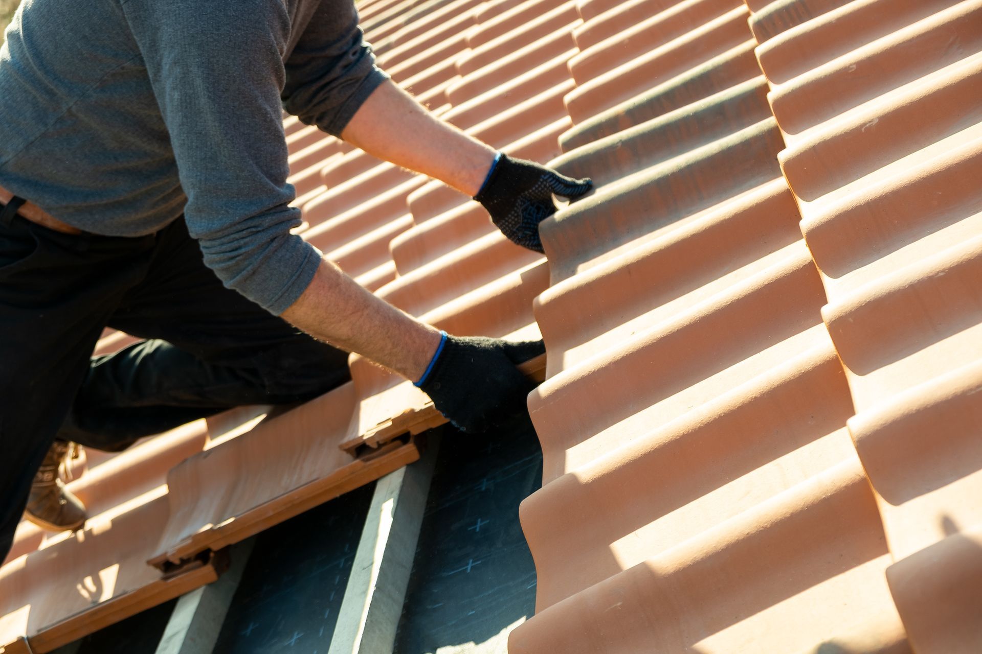 Person installing clay roof tiles on a wooden structure, wearing black gloves.