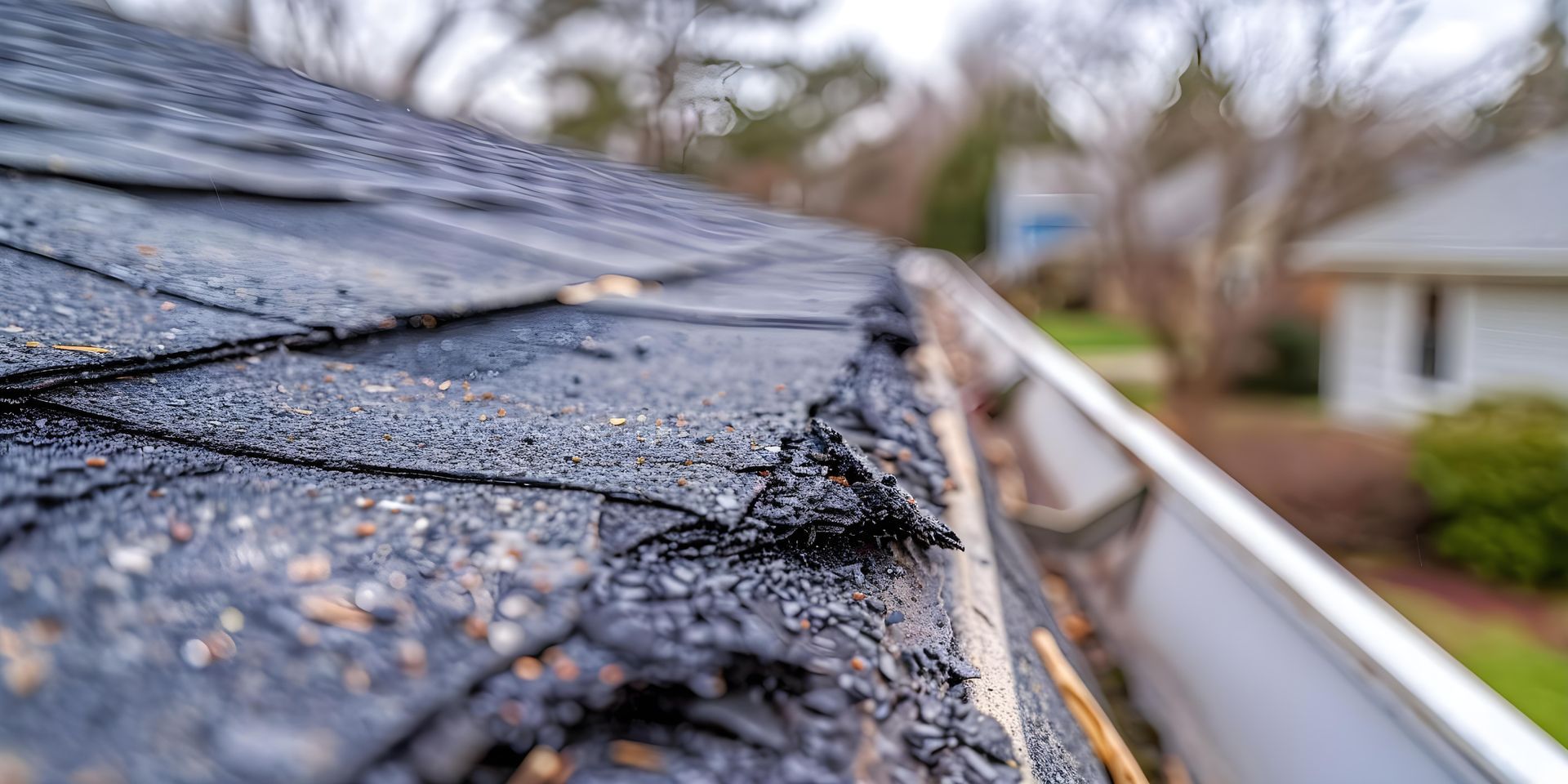 Close-up of a damaged roof with crumbling asphalt shingles and a gutter along the edge.