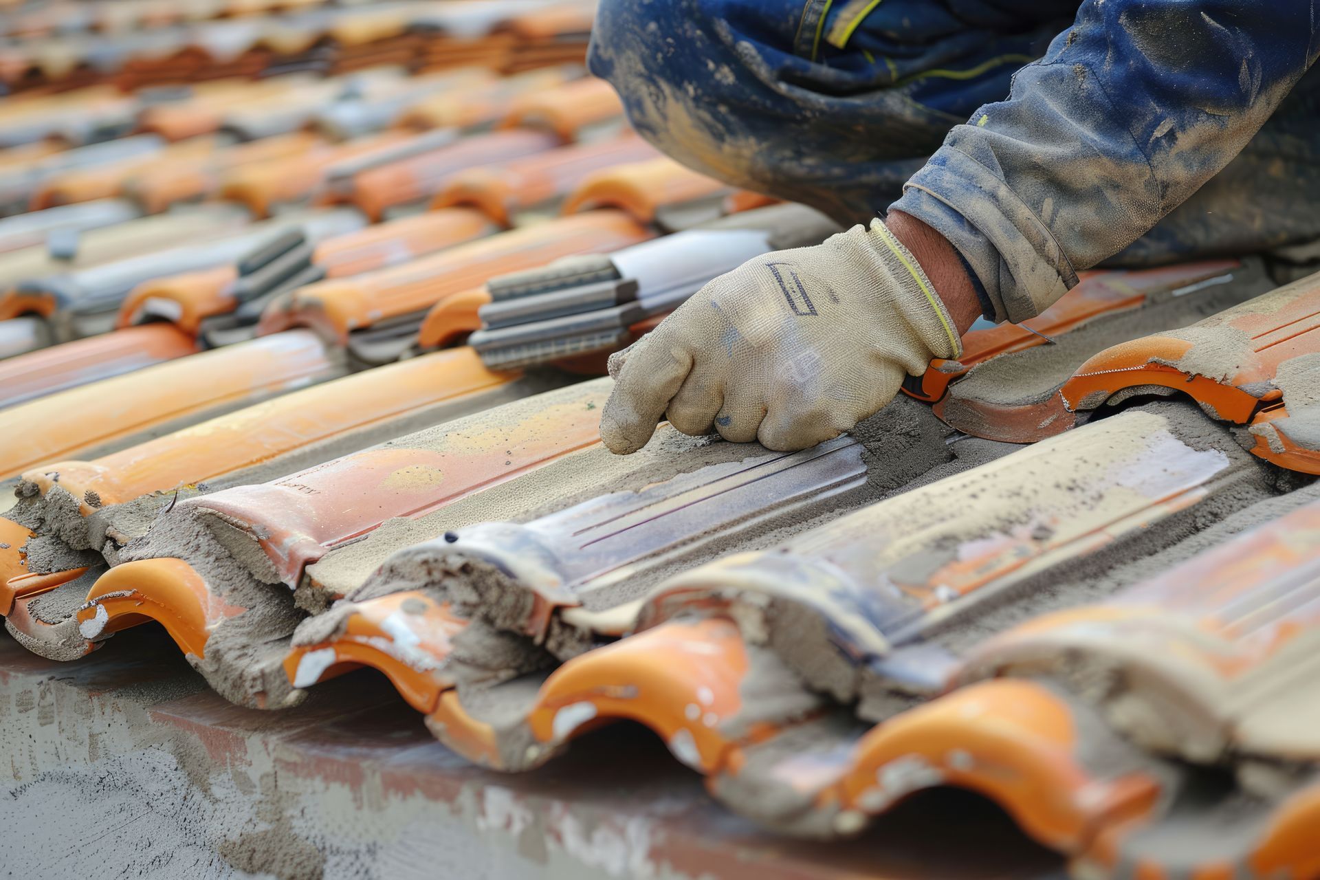 Person installing orange clay roof tiles; close-up of gloved hand and tiles.