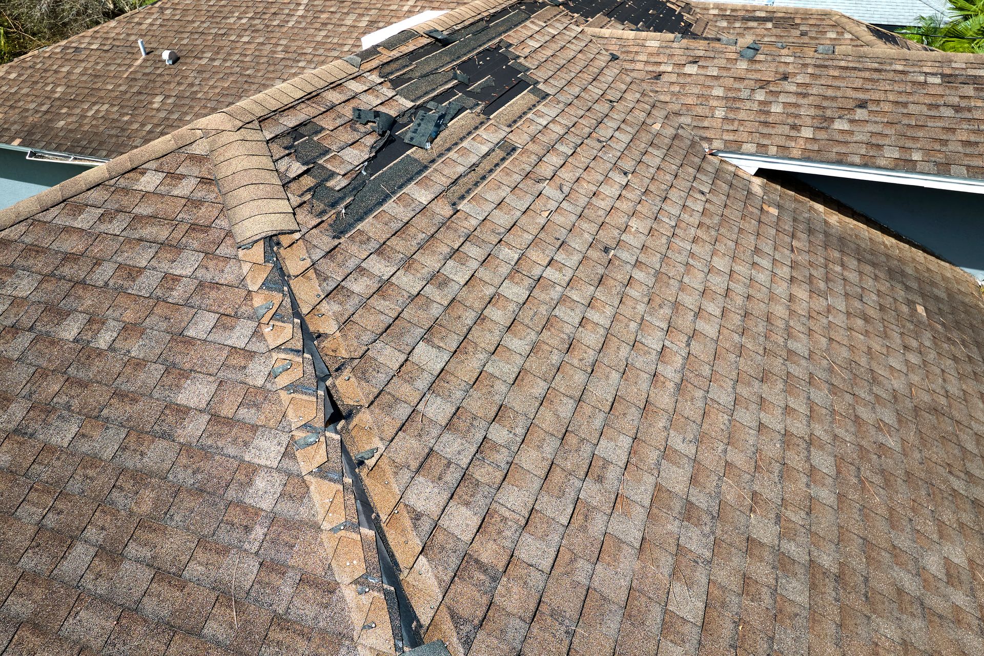 Damaged asphalt shingle roof, with missing shingles and exposed underlayment.