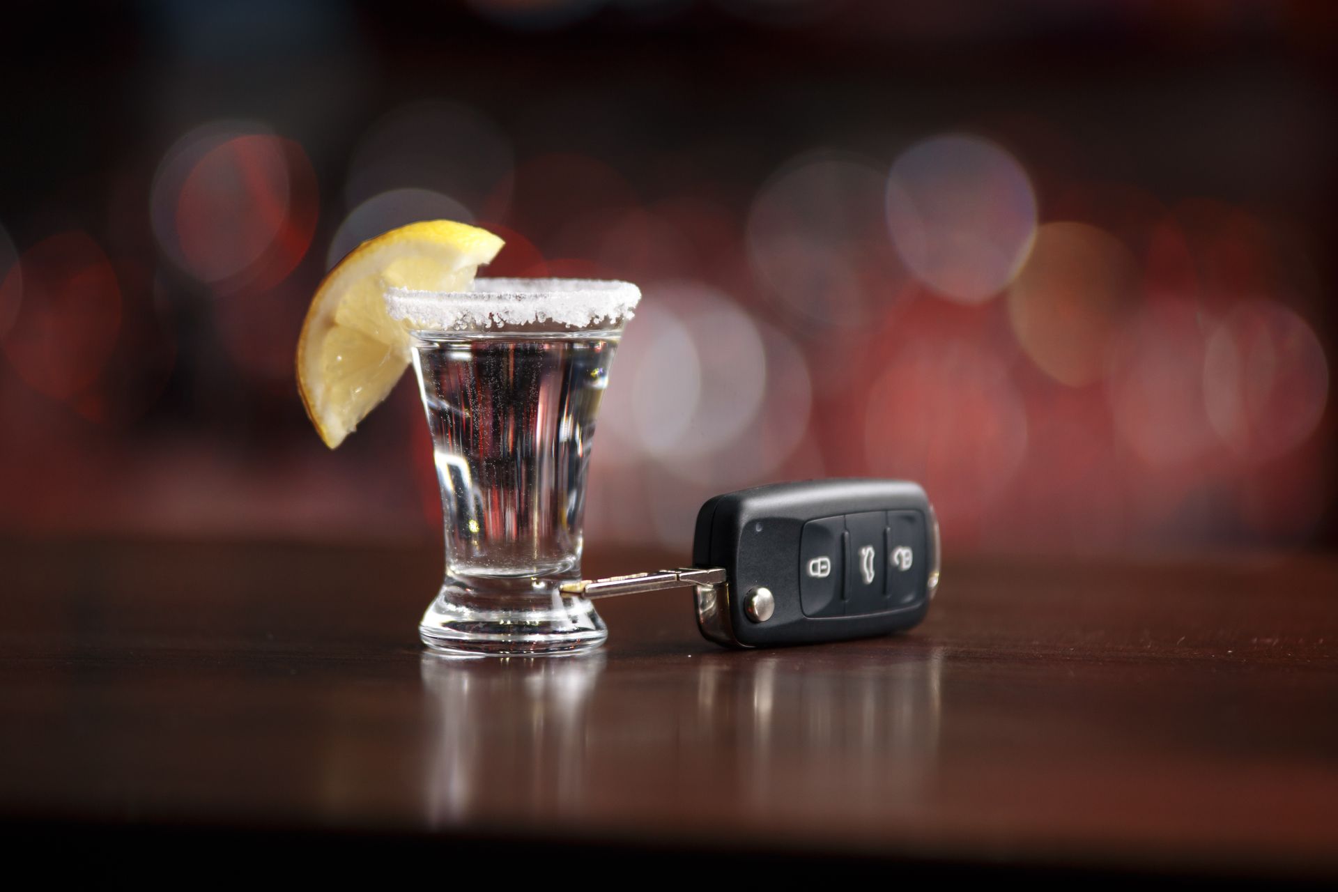 A shot of tequila with a slice of lemon and a car key on a table.