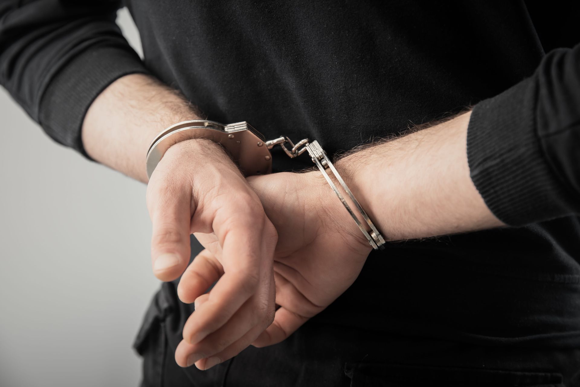 Handcuffed wrists in a dark shirt, suggesting arrest or detention.