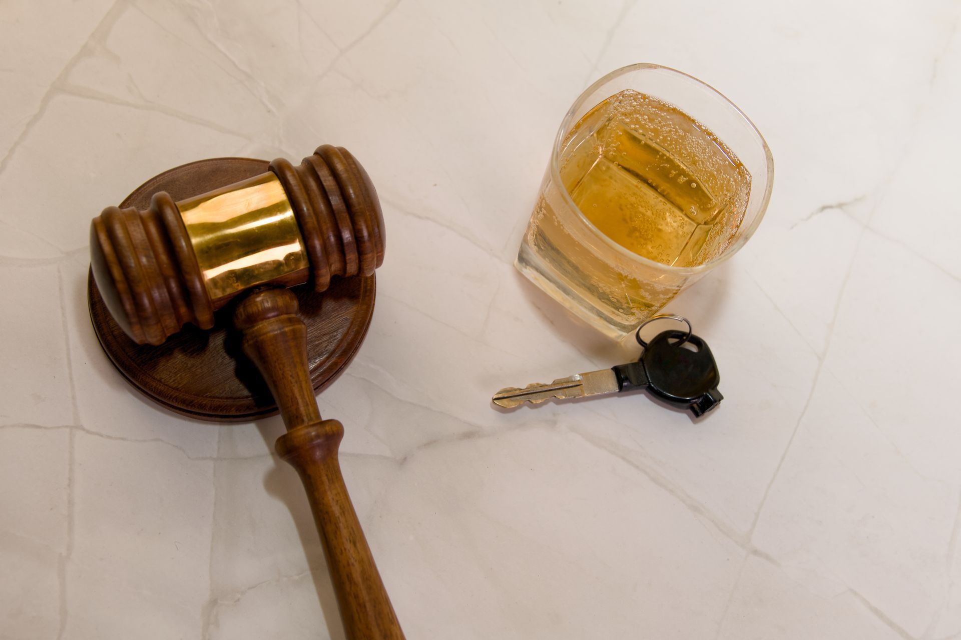 Gavel, glass of amber liquid, and car key, representing DUI in Coral Gables.