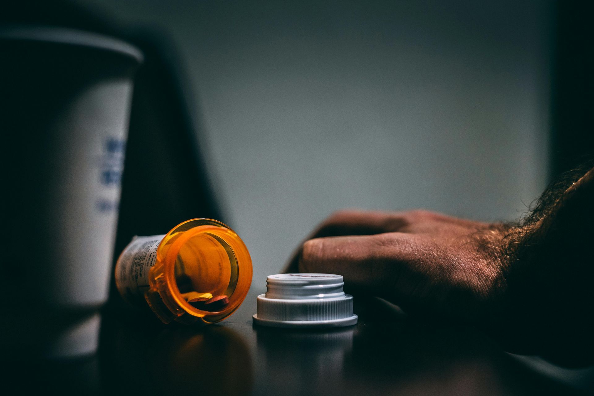 A person is holding a bottle of pills on a table.