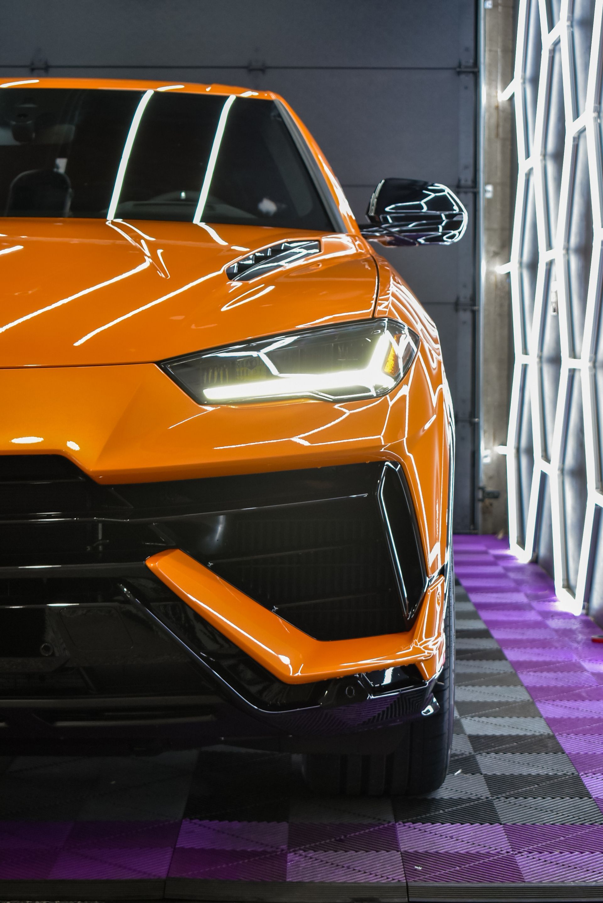 A close up of an orange lamborghini urus parked in a garage.