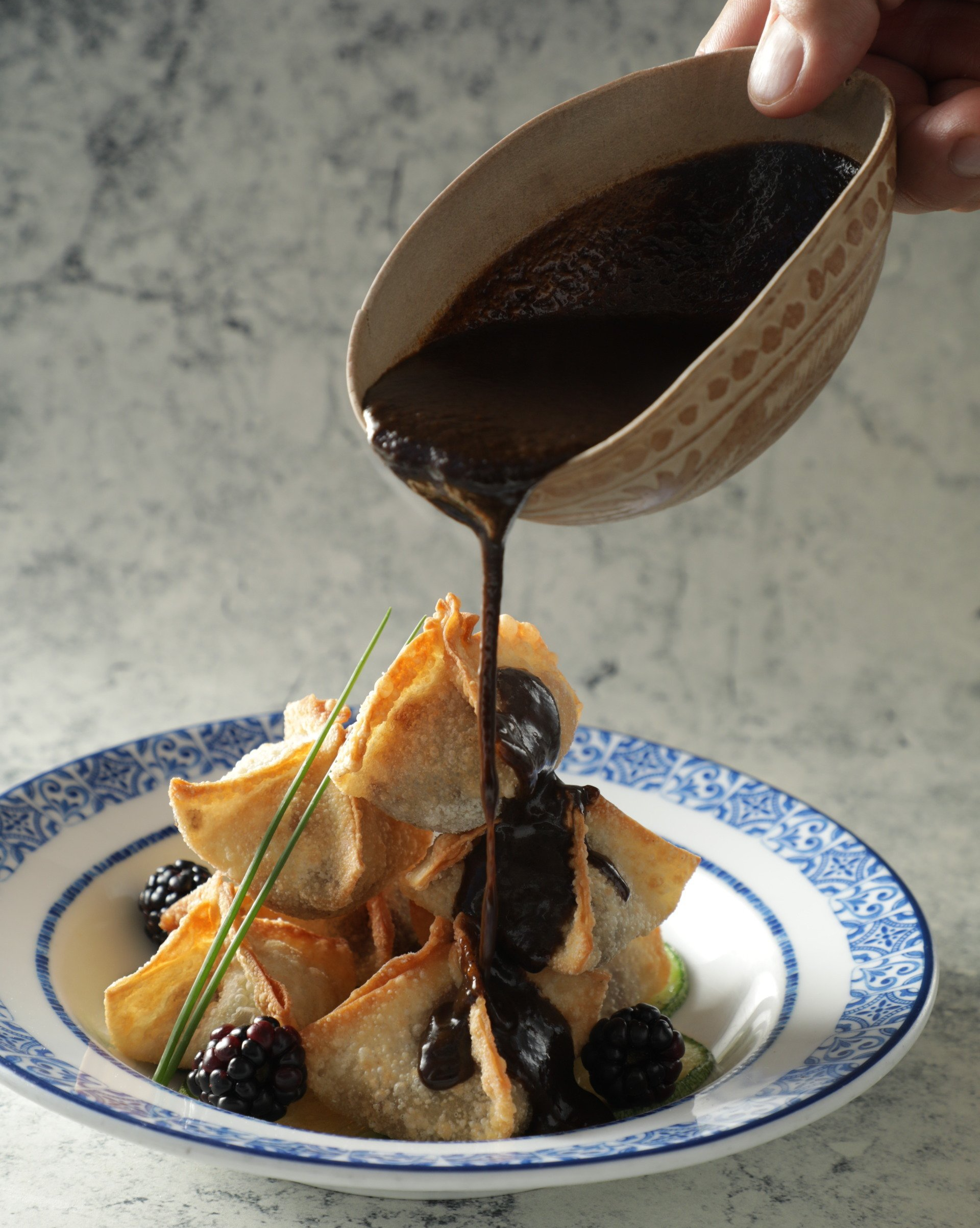 Crepe de postre cubierta con frutos rojos, rociada con salsa oscura de un tazón.