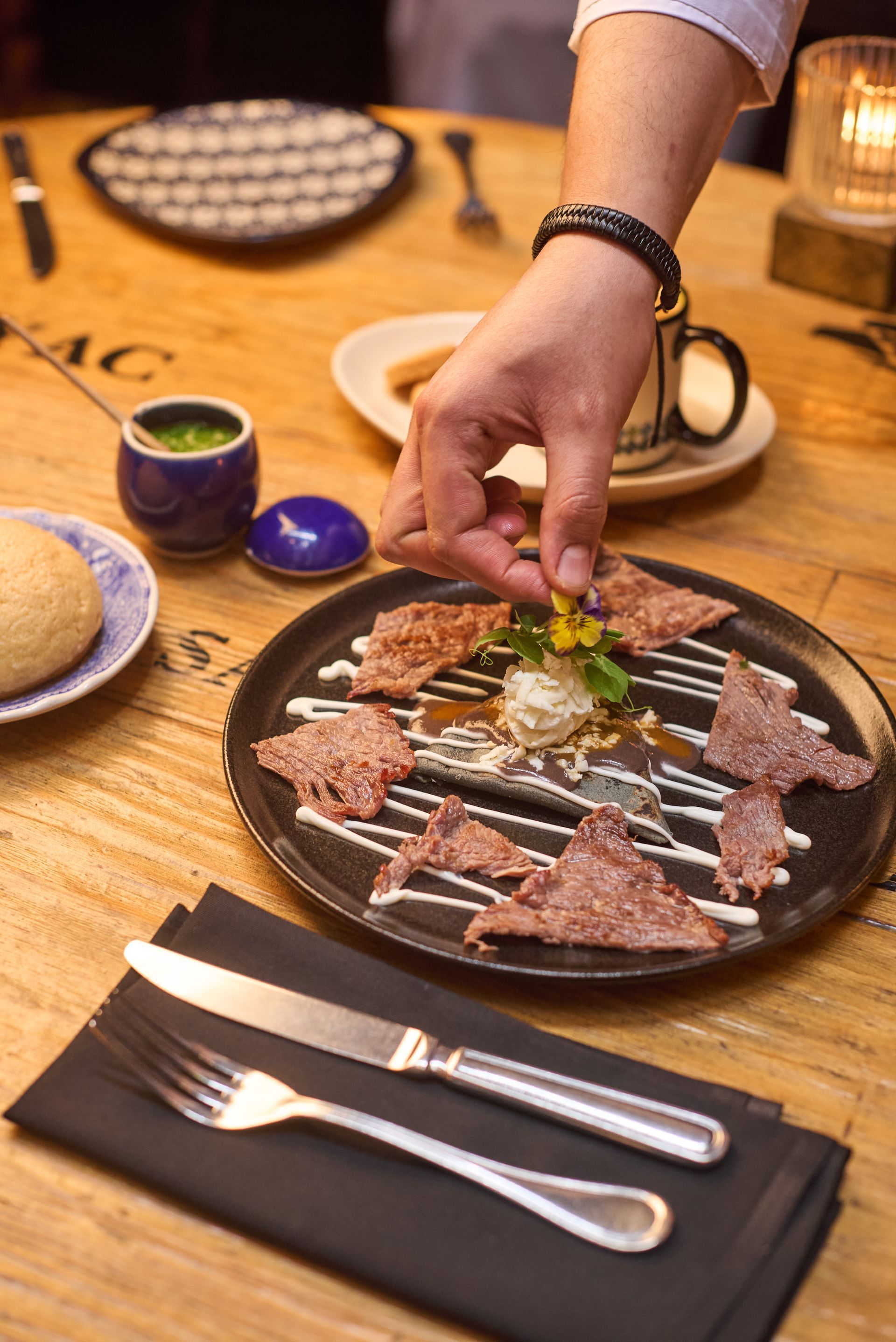 Colocación manual de una guarnición en una fuente de carne a la parrilla en una mesa de restaurante.
