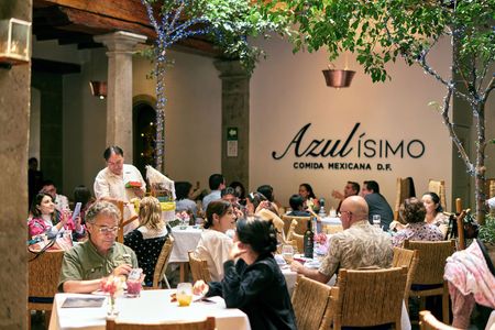Gente cenando en mesas en un restaurante con iluminación cálida y un letrero que dice 