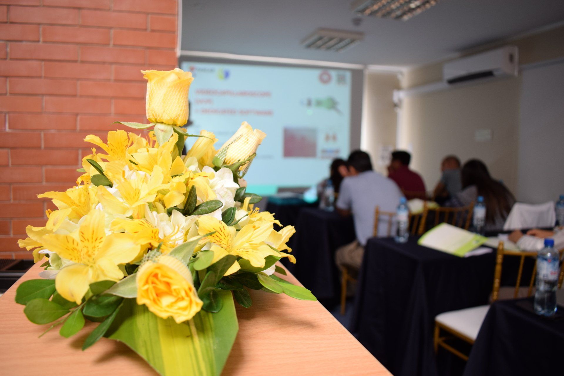 Un ramo de flores amarillas está sobre una mesa frente a una pantalla de proyector.