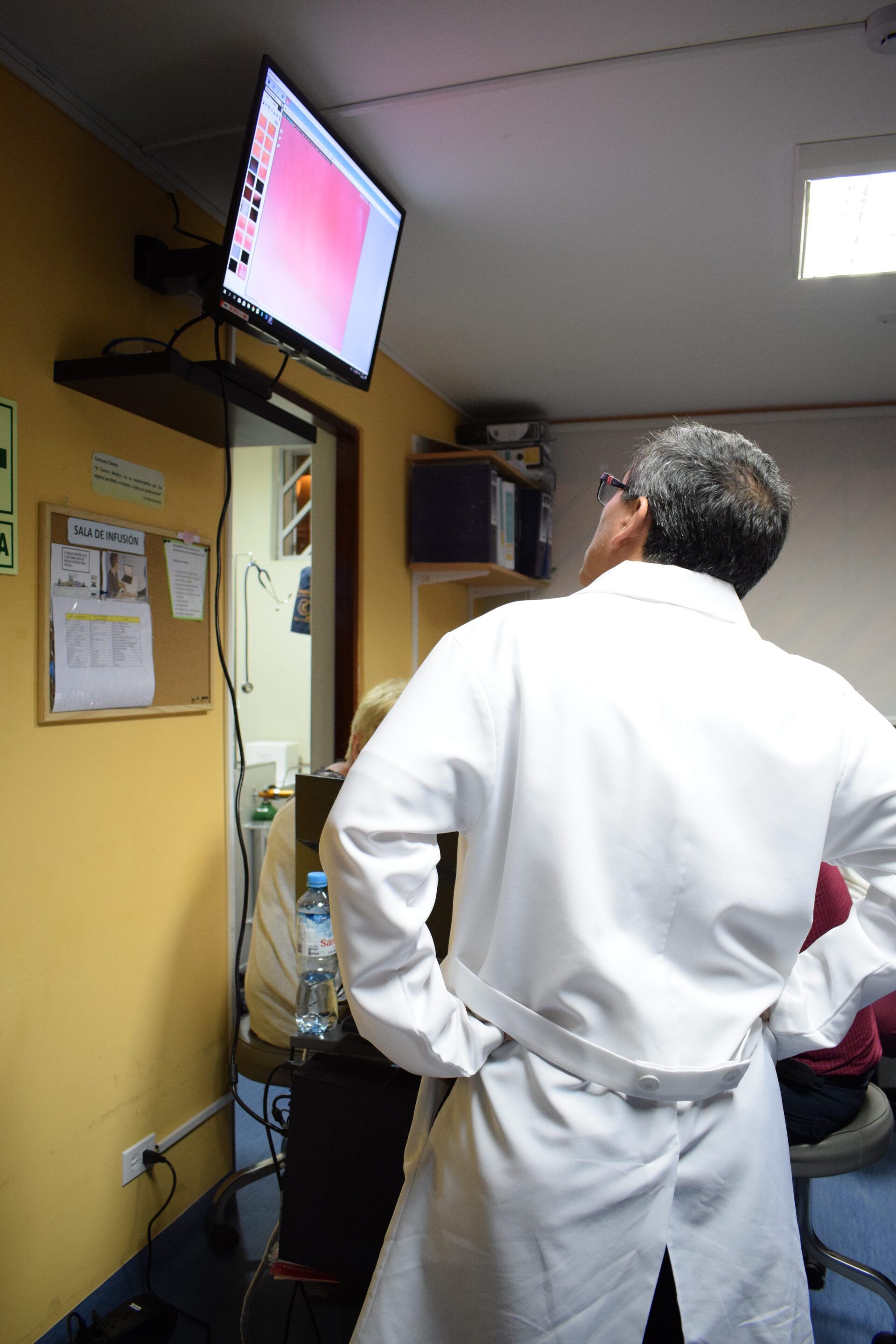 Un hombre con bata de laboratorio está parado frente a un televisor.
