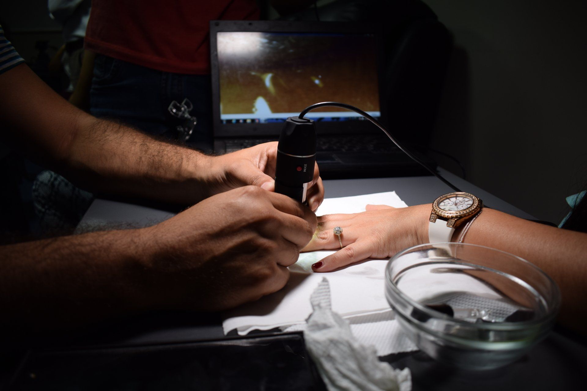 Un hombre pinta las uñas de una mujer frente a una computadora portátil.