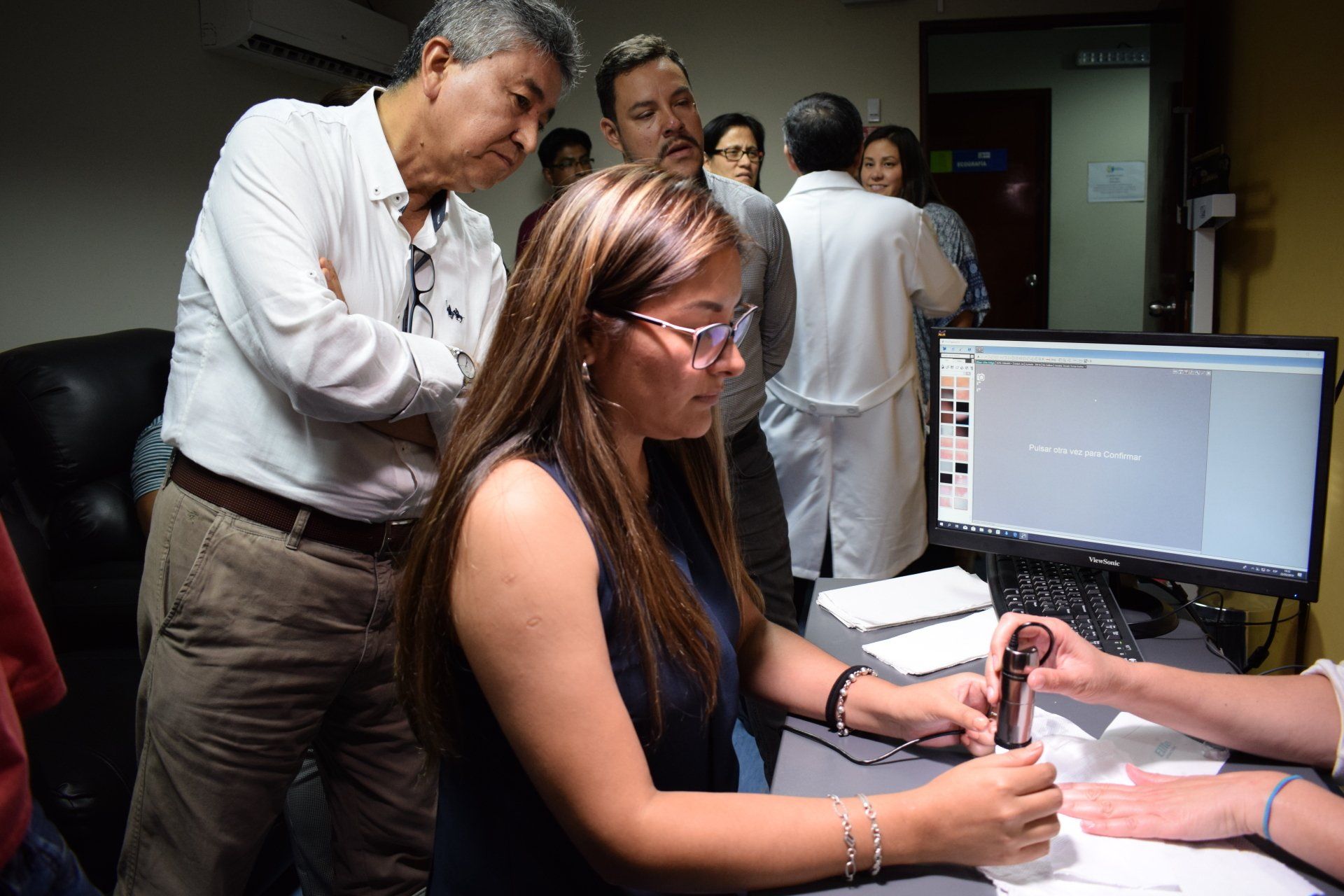Un grupo de personas está de pie alrededor de una mujer sentada en un escritorio frente a una computadora.