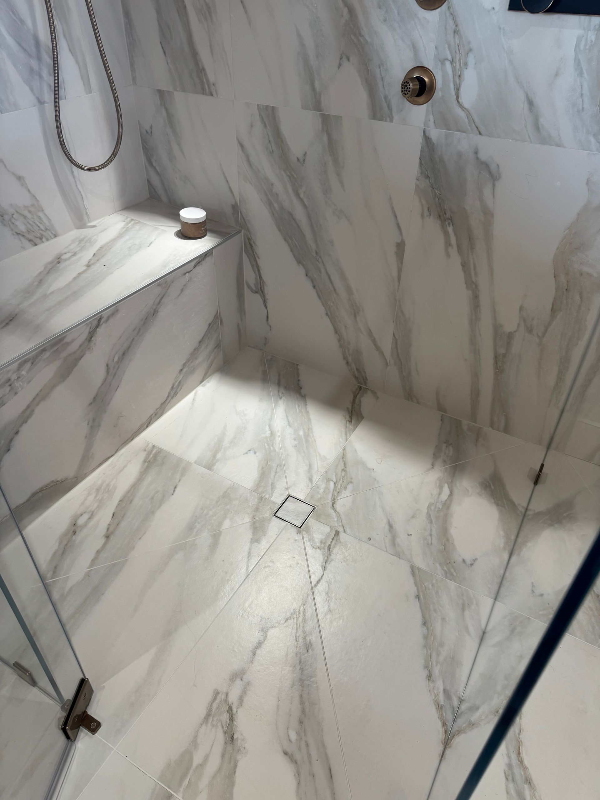 Shower with white marble-patterned tile, featuring a built-in bench and a central drain.