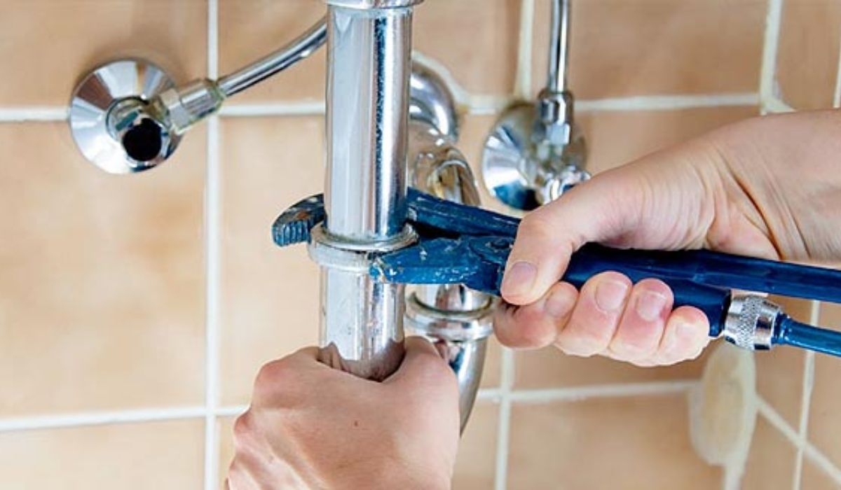 a pair of hands repairing a sink pipe with a pipe wrench