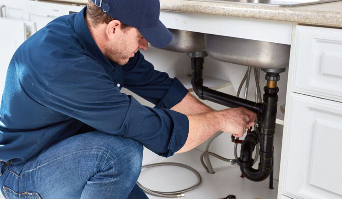a man repairing the pipes under a kitchen sink