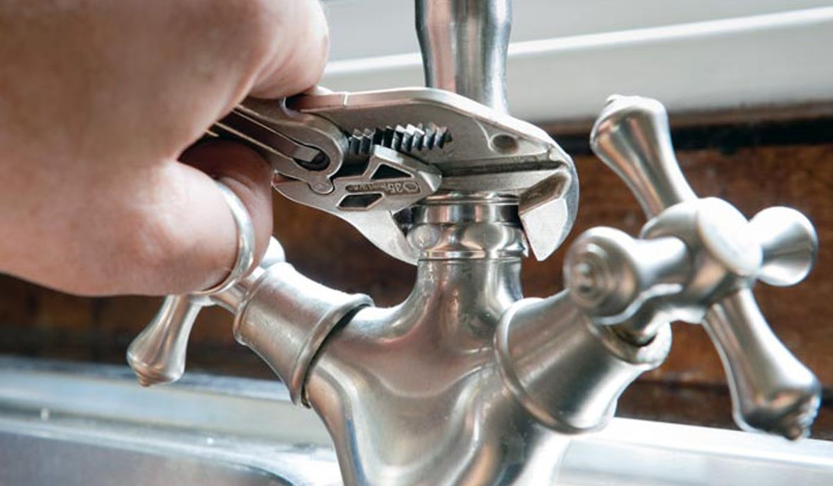 a man's hand repairing faucet using wrench