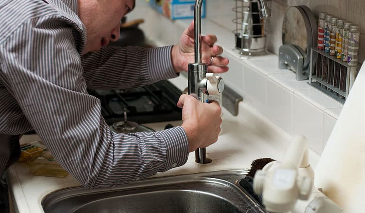 a man fixing the sink faucet in the kitchen
