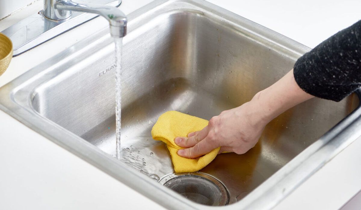 scrubbing sink clean with yellow sponge