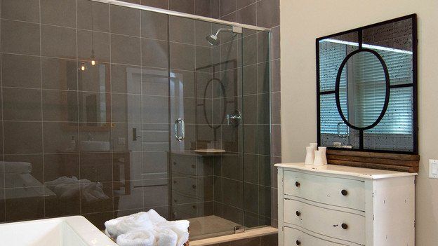 A bathroom with a walk in shower , sink , dresser and mirror.