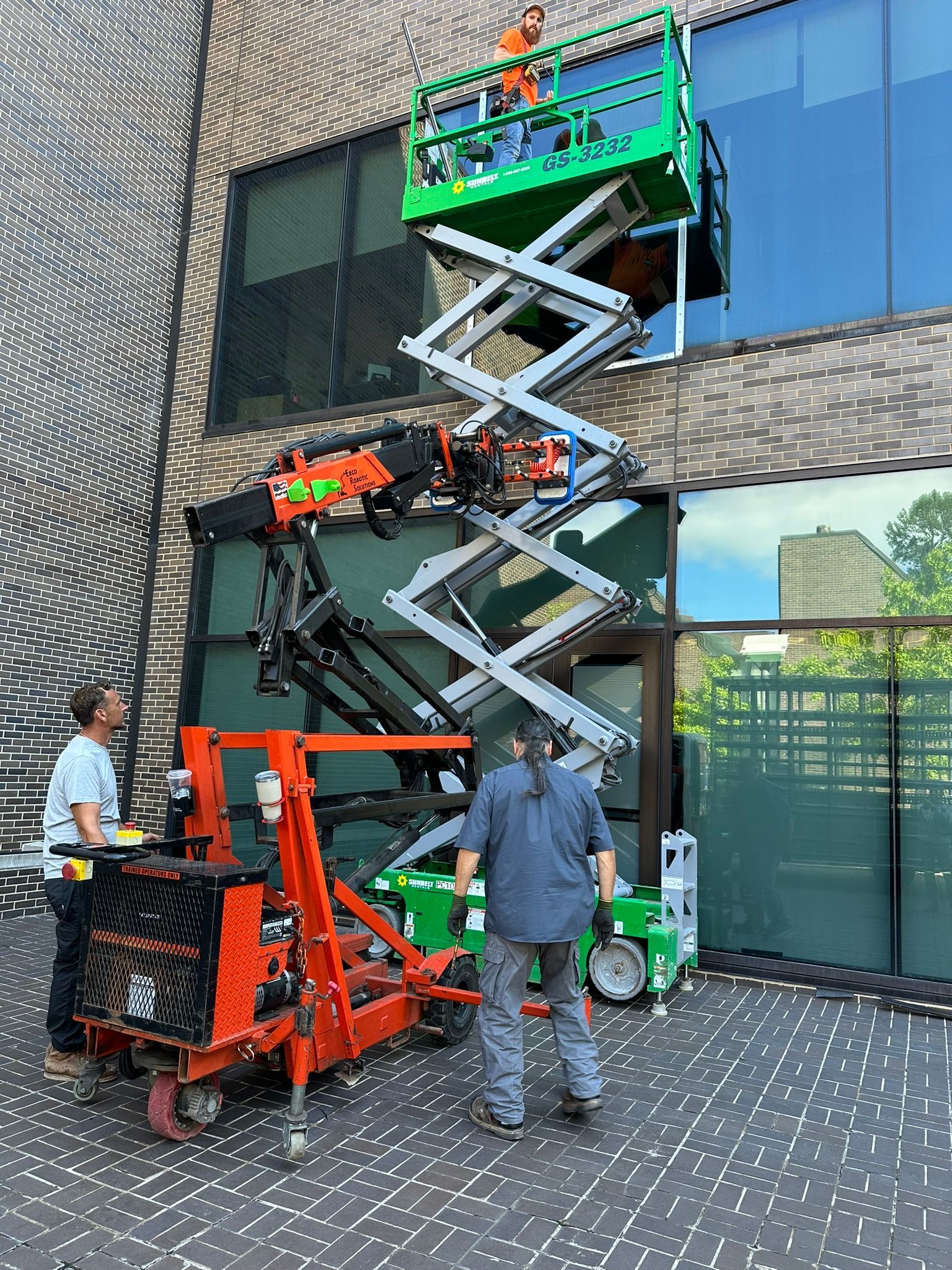 A man is standing next to a scissor lift in front of a building.
