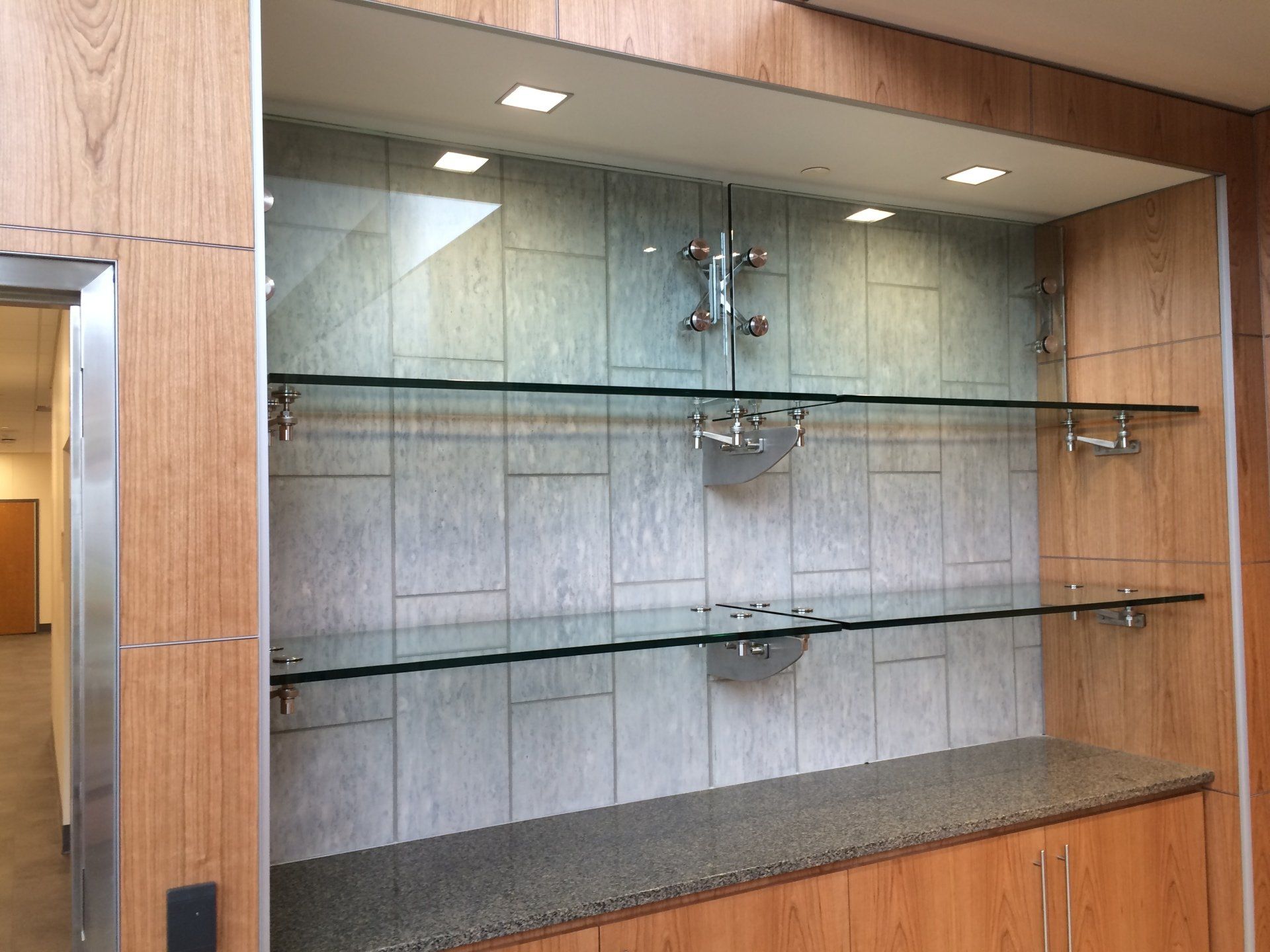 A shelf with glass shelves in a room with wooden cabinets.