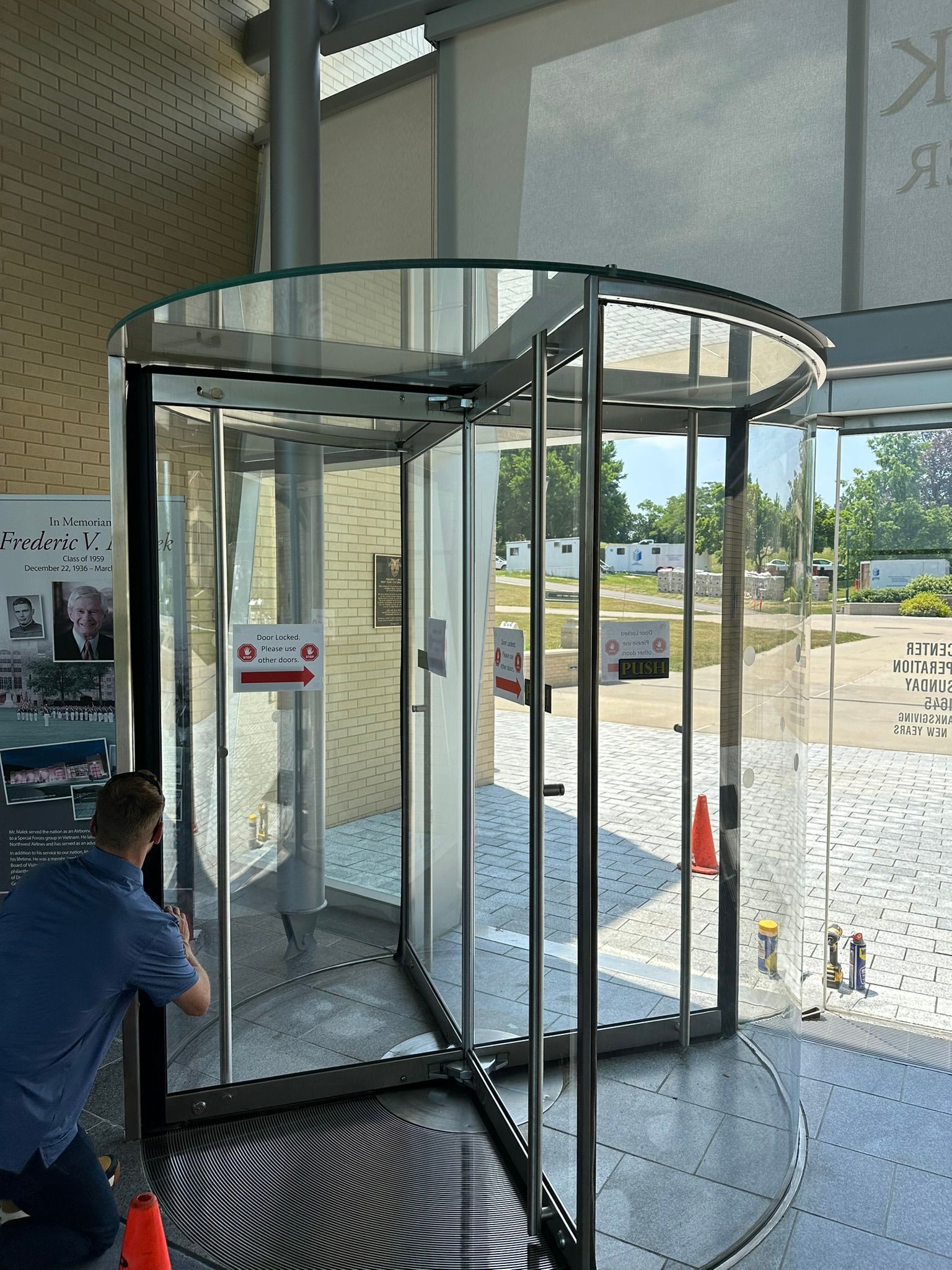 A man is standing in front of a glass revolving door.