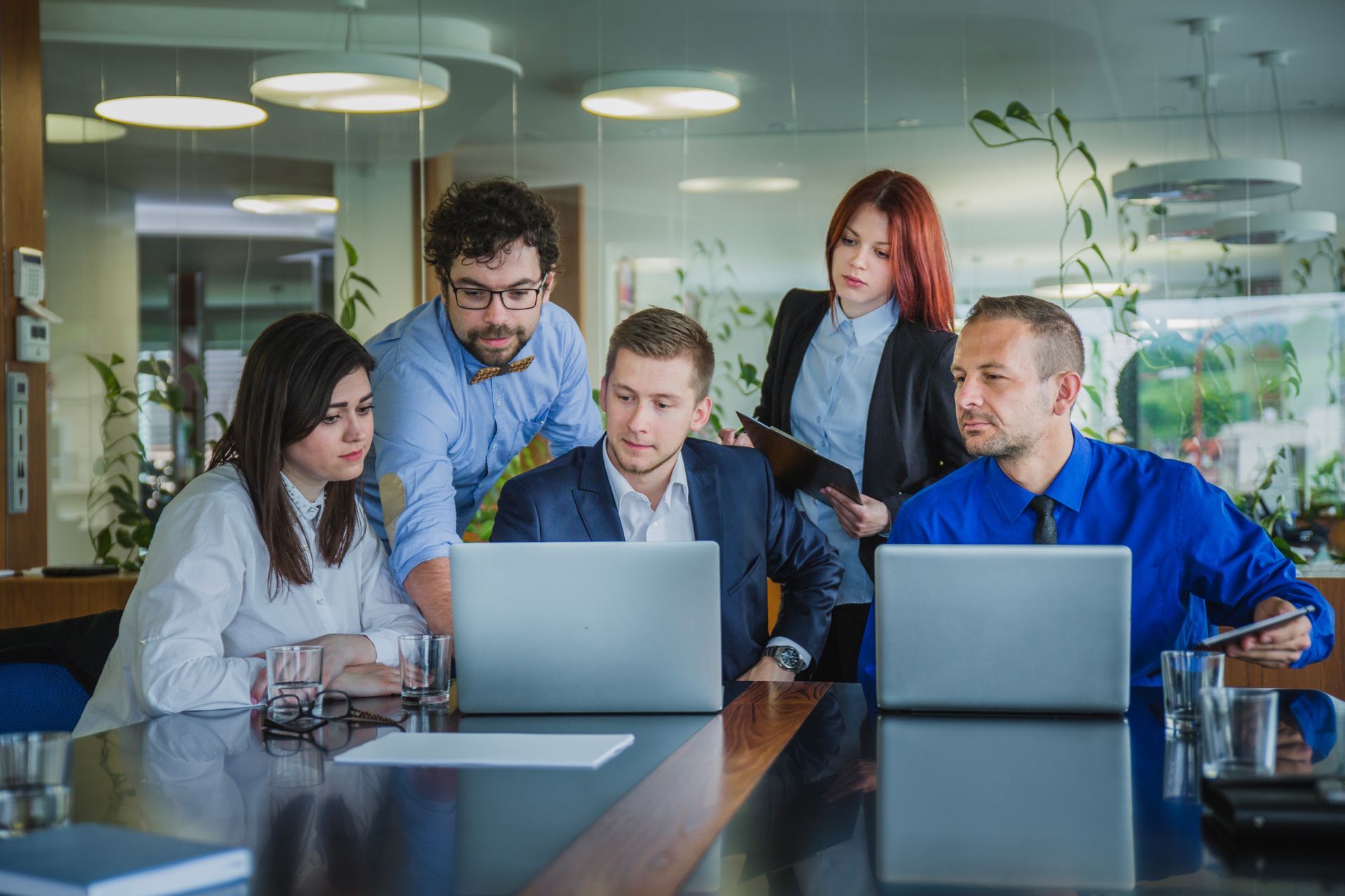 People around a table looking at a laptop in a modern office, discussing.