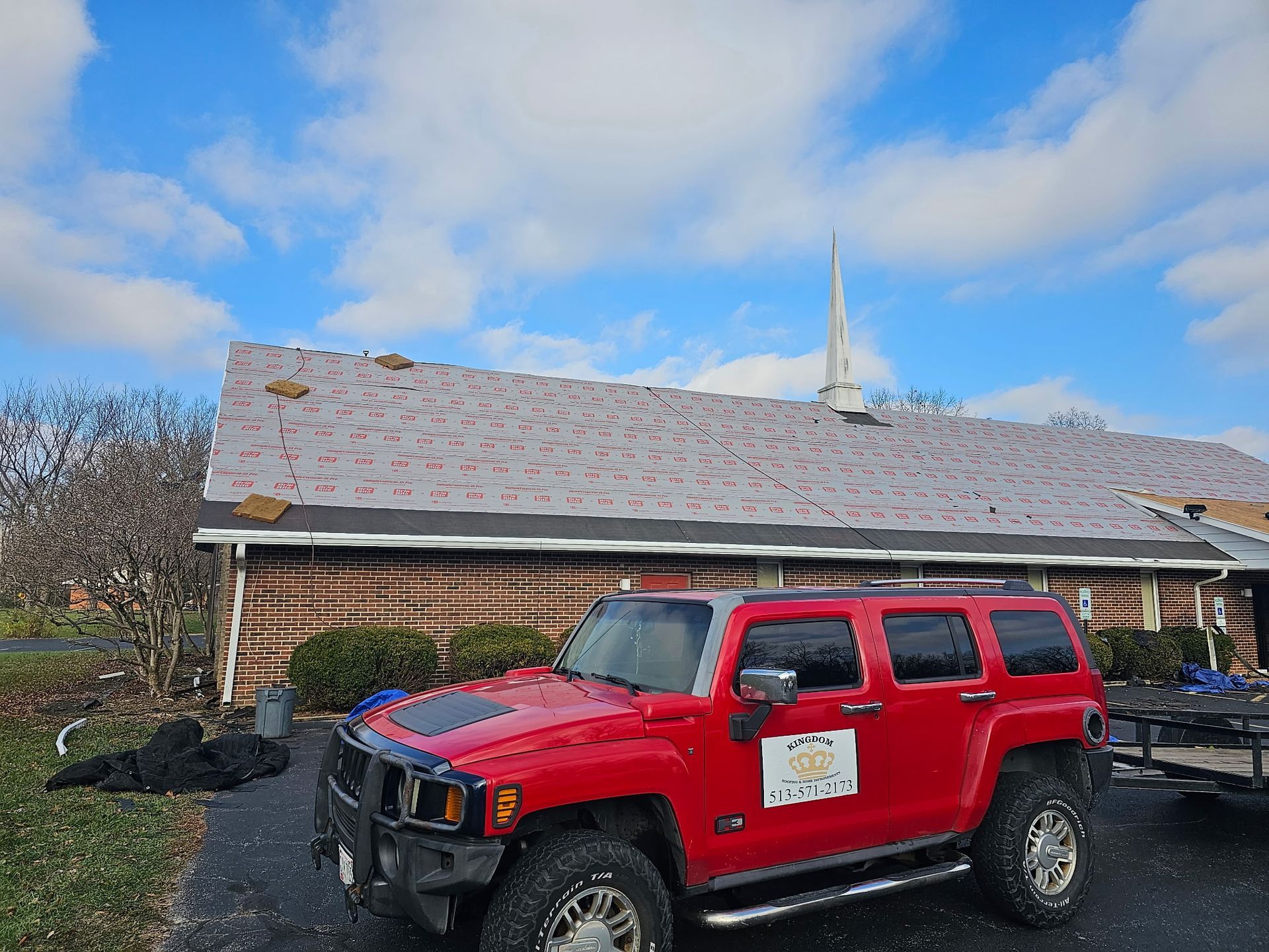 Red Hummer SUV in front of a building with a damaged roof under a cloudy sky.