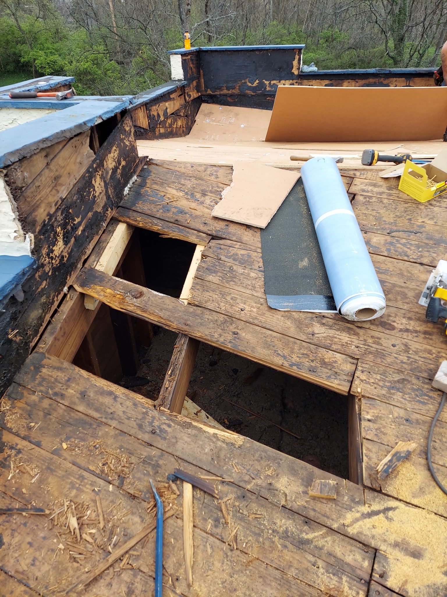 Roof repair in progress; exposed wooden structure, open holes, tools, blue tarp, and insulation.