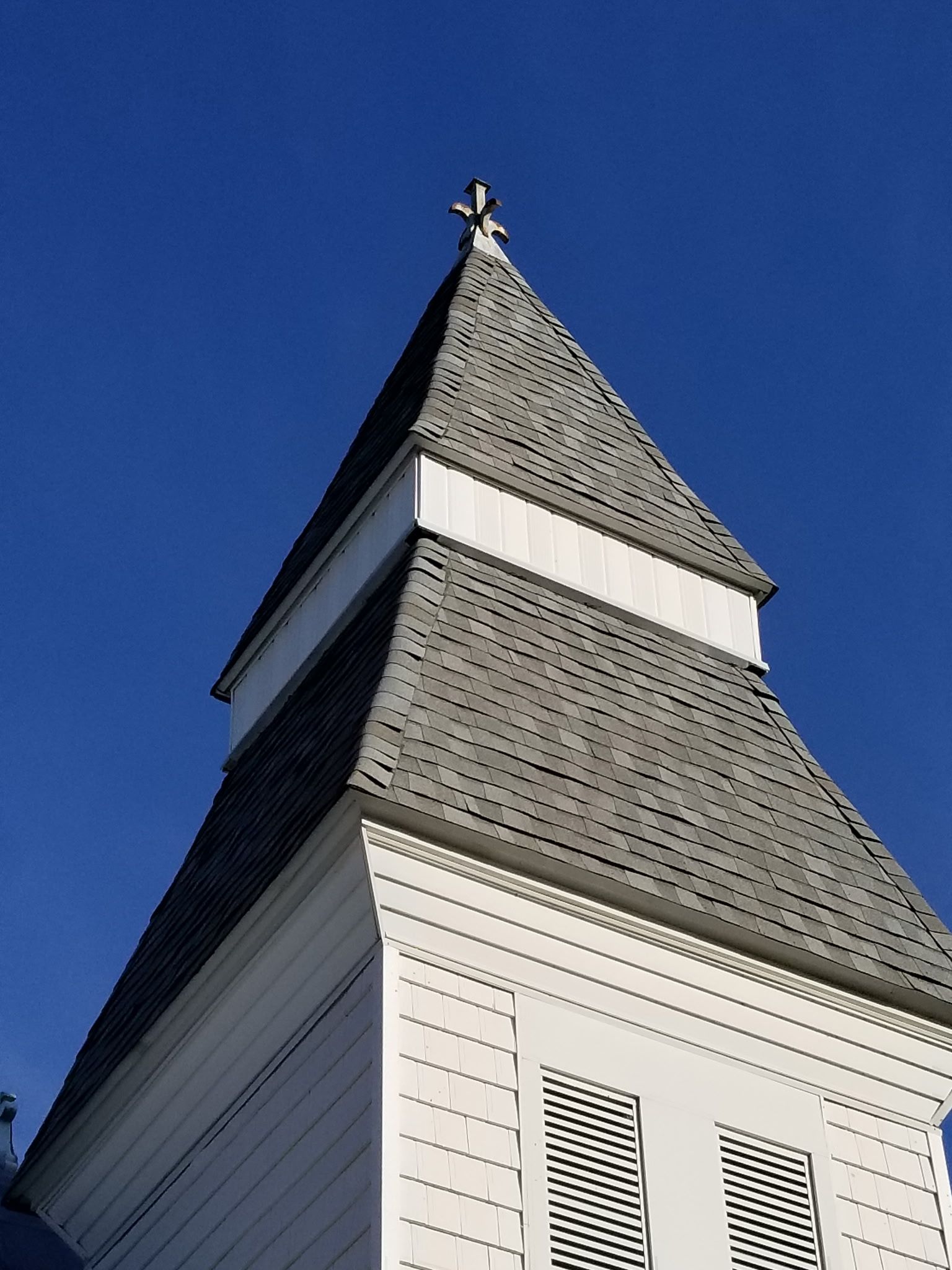 White church steeple with gray shingle roof against a clear blue sky.