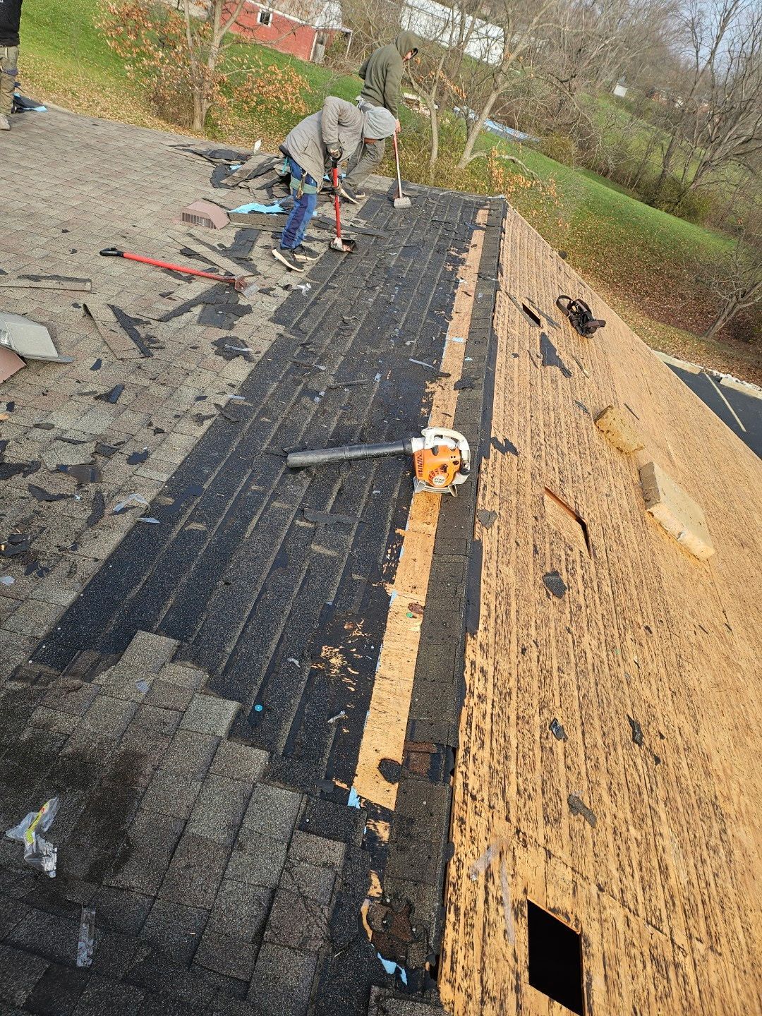 Two people installing siding on a building's exterior near a window, one using a nail gun.
