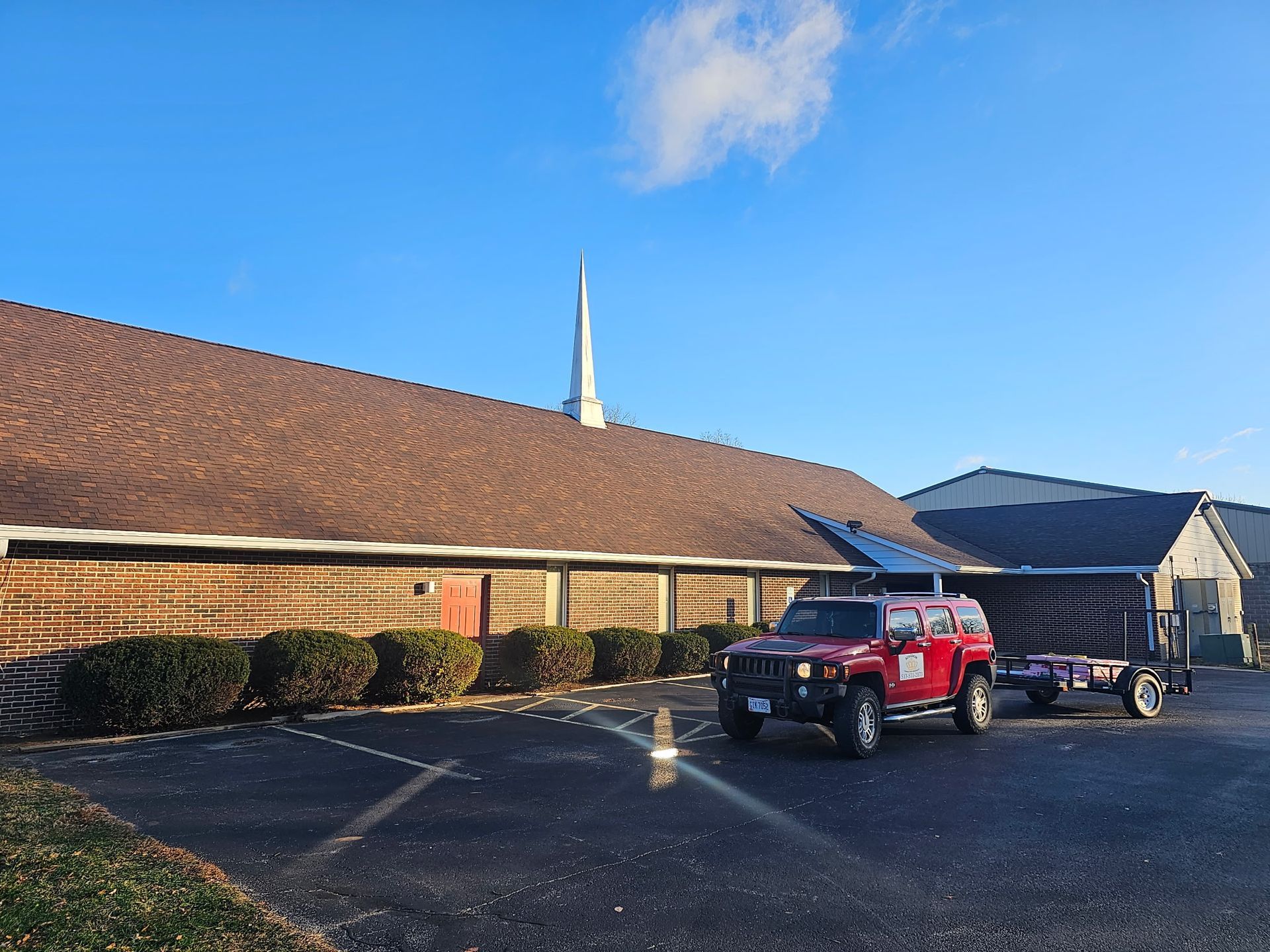 Damaged house roof covered with blue tarp, white siding, cloudy sky, tree in the background.