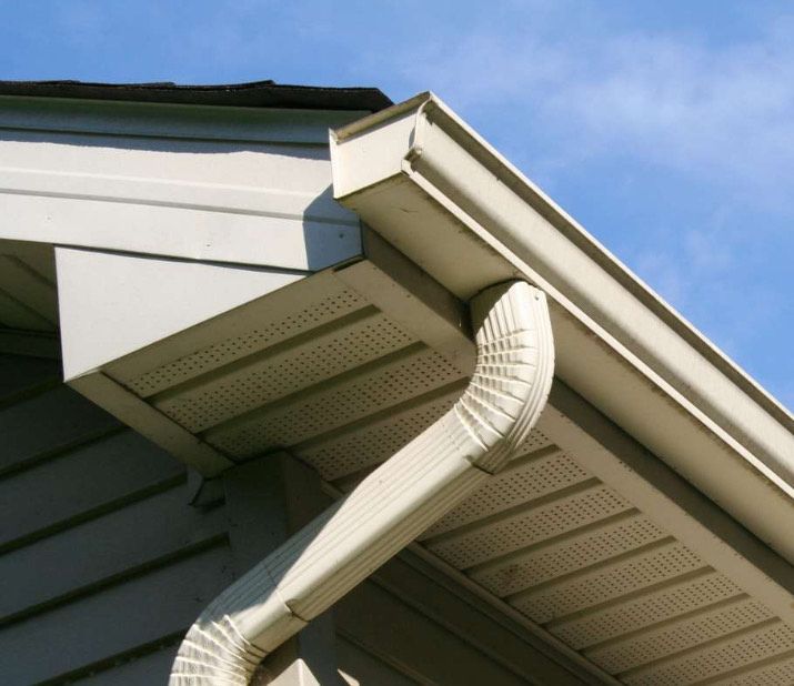 White gutter system on a building's roof corner, angled against a blue sky.