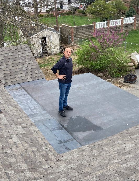 Siding partially removed from a house, revealing plywood sheathing. A ladder rests against the wall.