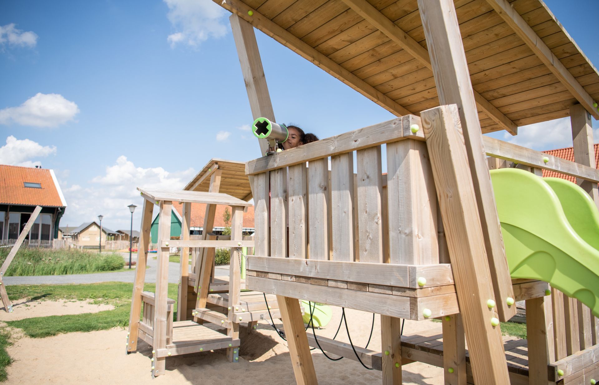 A child is playing on a wooden playground with a green slide.