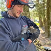 A man is holding a small squirrel in his arms.