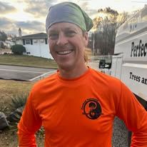A man wearing a bandana and an orange shirt is standing in front of a truck.