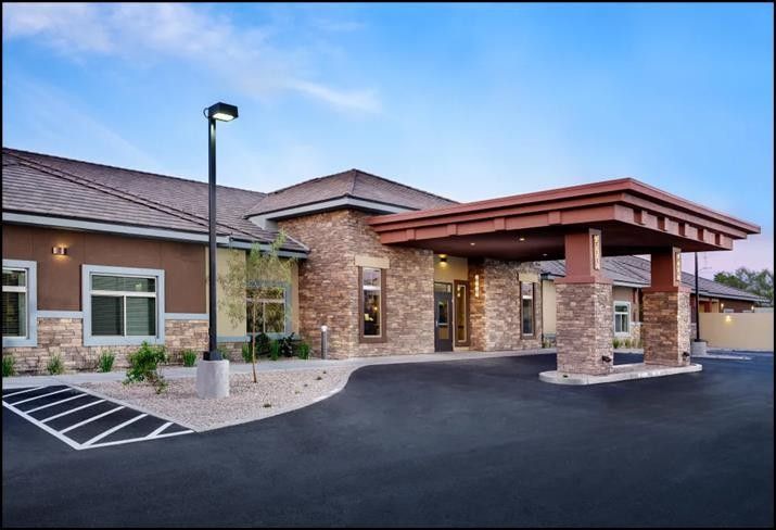 Building entrance with stone facade, dark asphalt driveway, and covered entry under a blue sky.