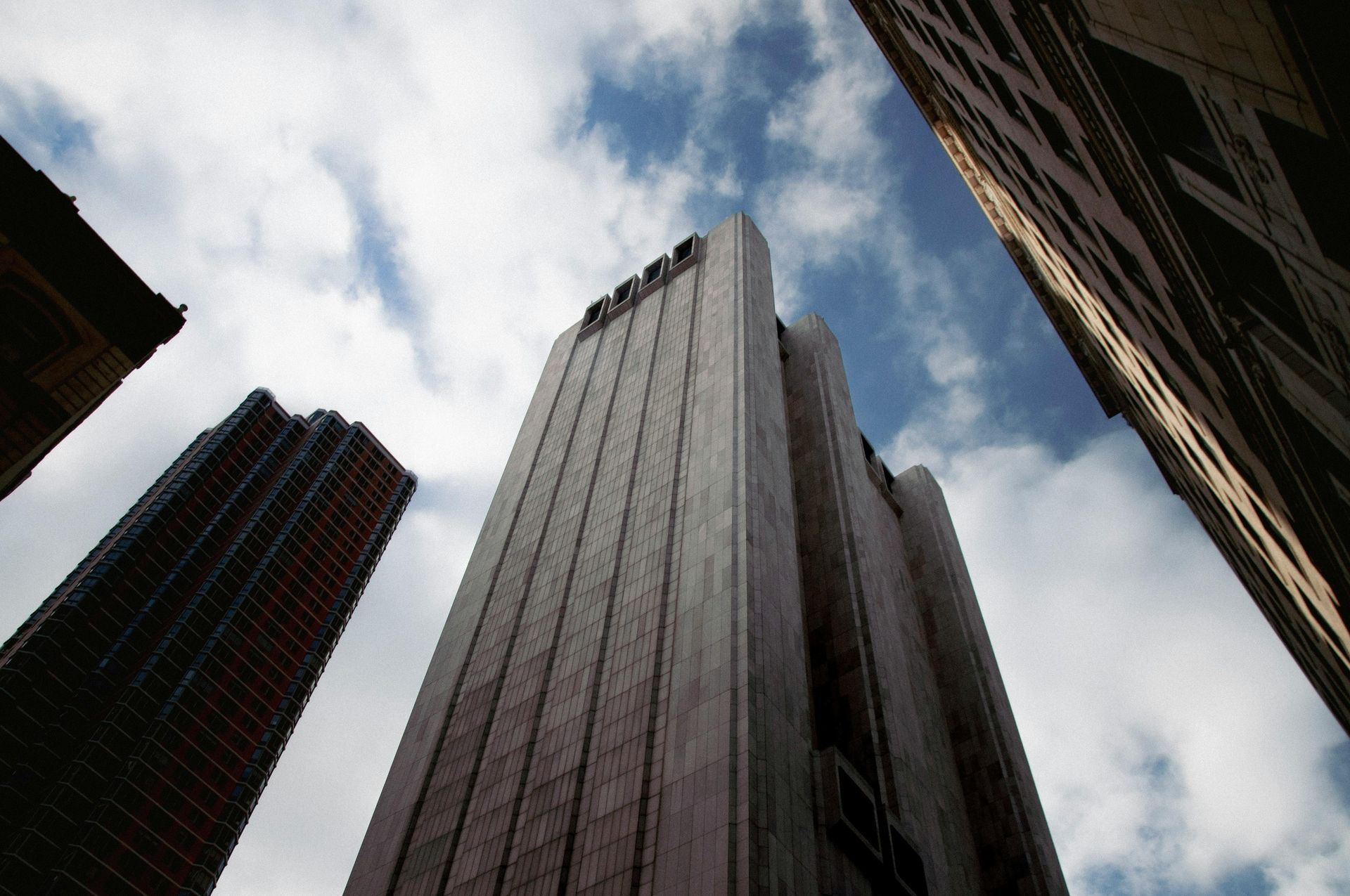 Looking up at tall buildings against a cloudy sky.