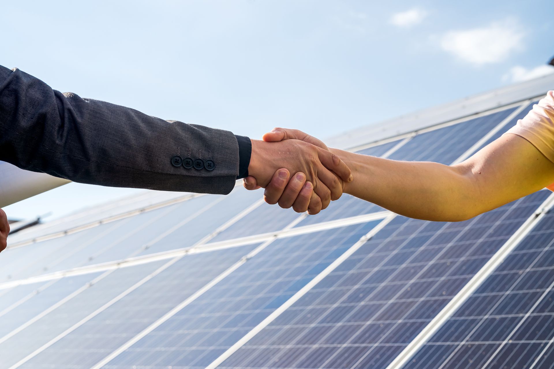 A man and a woman are shaking hands in front of a solar panel.