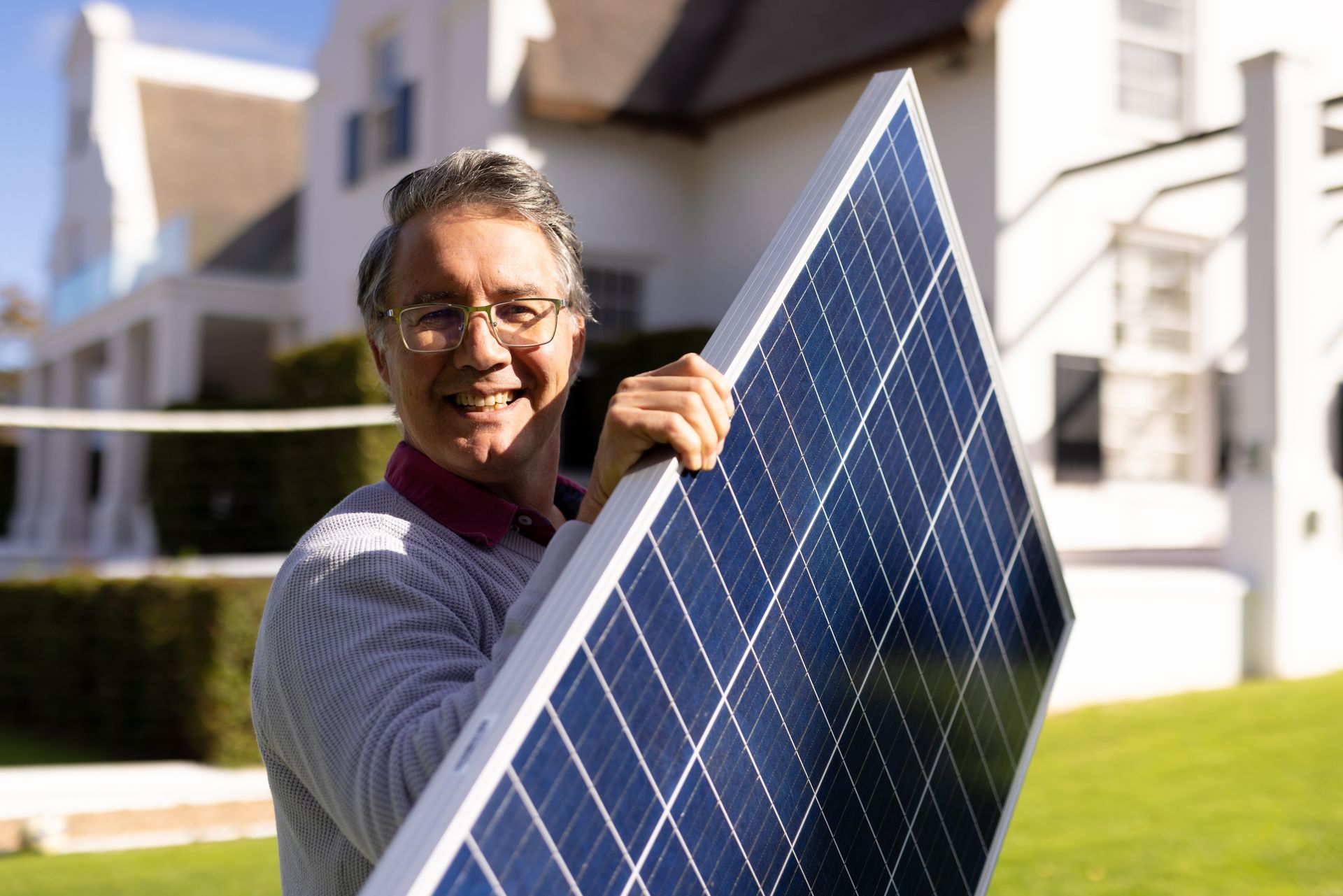 A man is holding a solar panel in front of a house.
