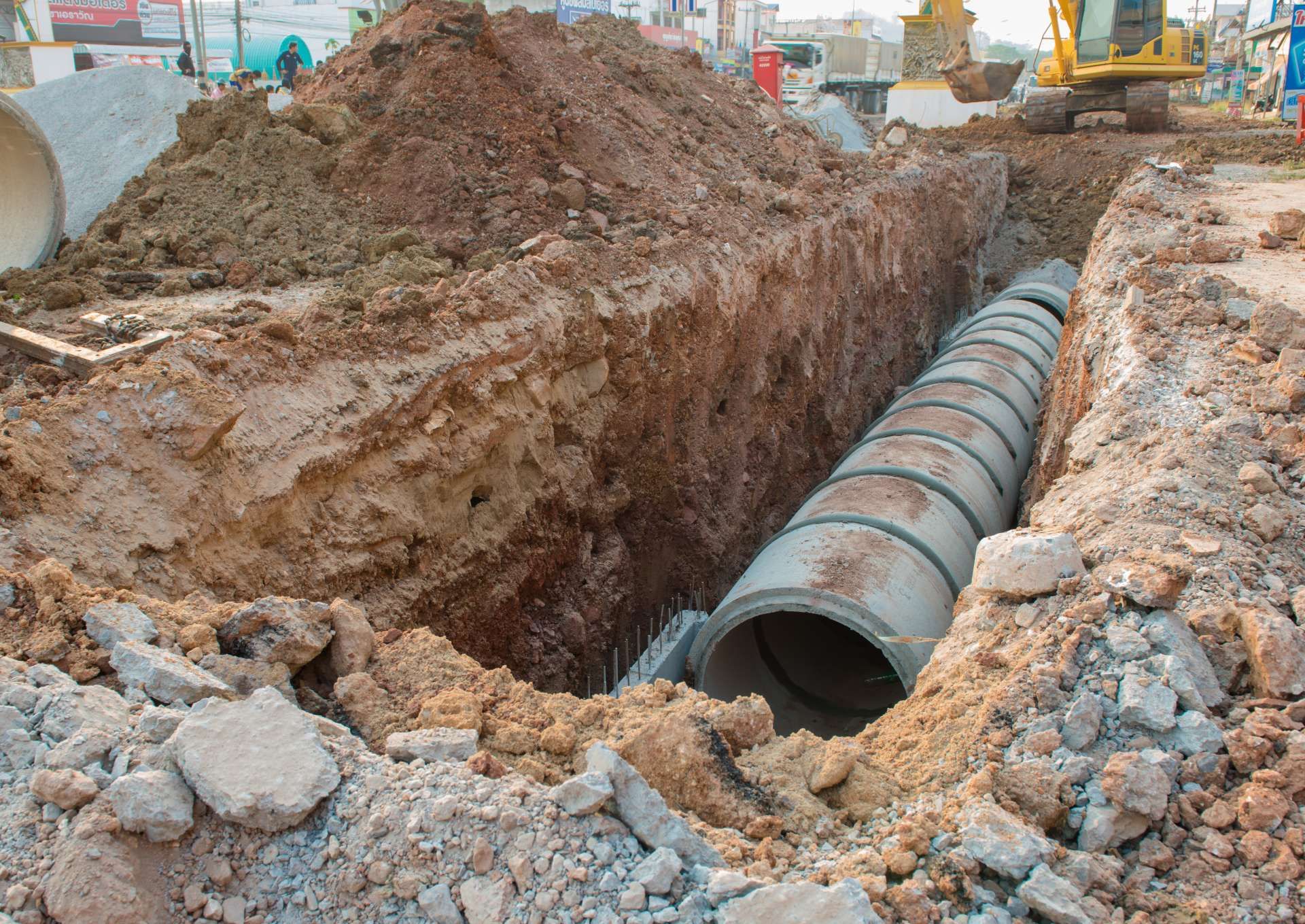 Excavated trench with large buried pipe sections at a construction site, surrounded by dirt and rocks