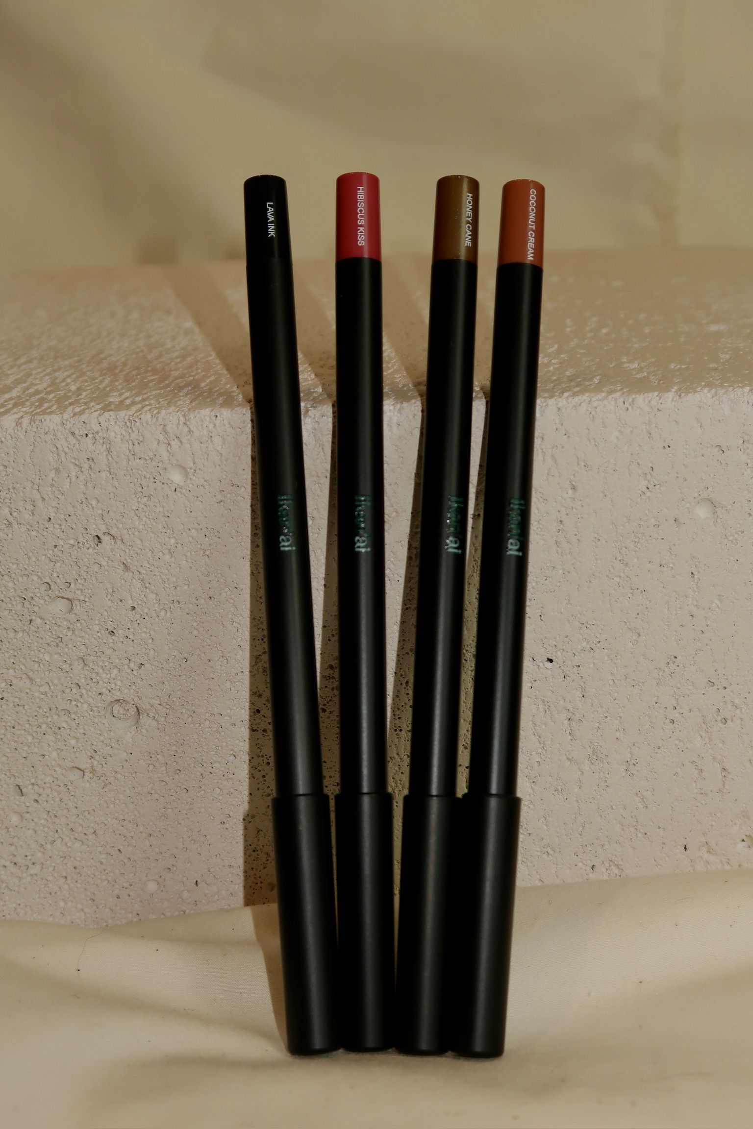 Four black lip pencils in varying shades of red and brown, resting on a beige ledge — Ikan'ai In Bowral, NSW
