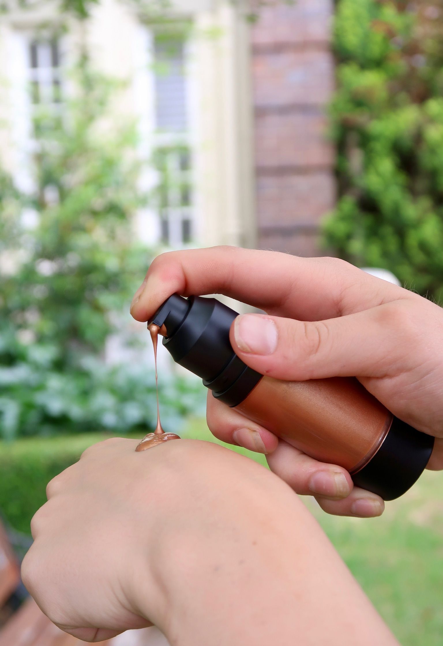 Person dispenses foundation from a brown pump bottle onto their wrist, outdoors  — Ikan'ai In Bowral, NSW