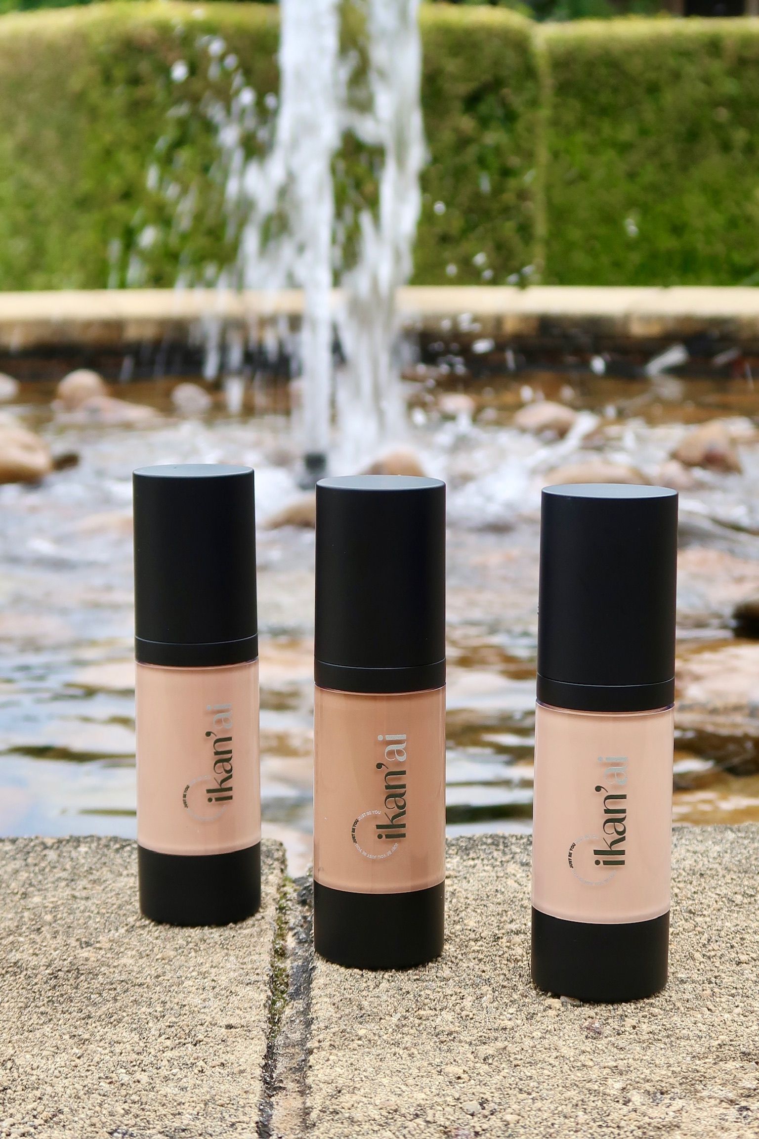 Three cosmetic product containers in front of a fountain; each is beige and black, with a white label  — Ikan'ai In Bowral, NSW