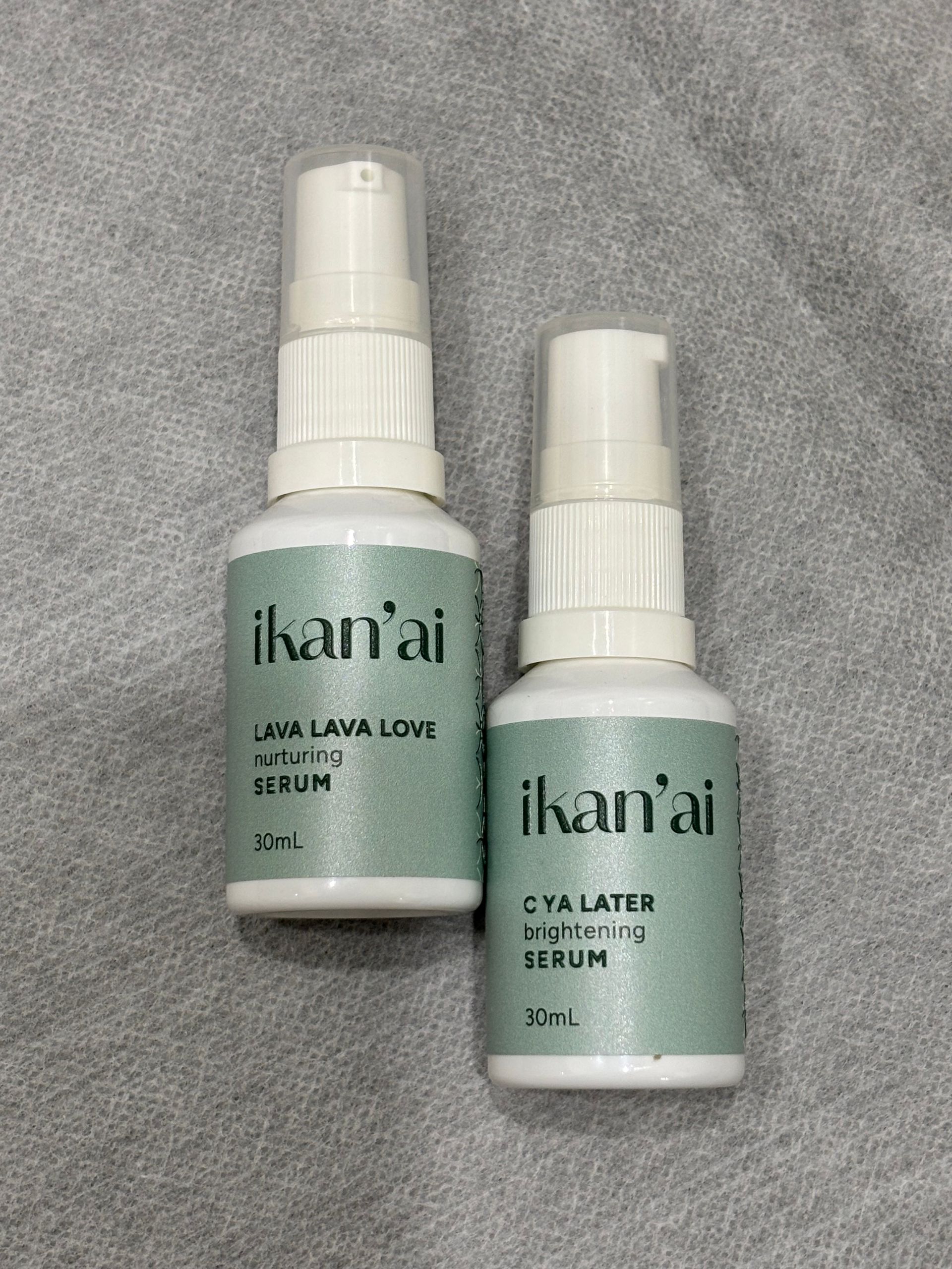 Two white bottles of Ikan'ai skin serum on a gray surface. One reads