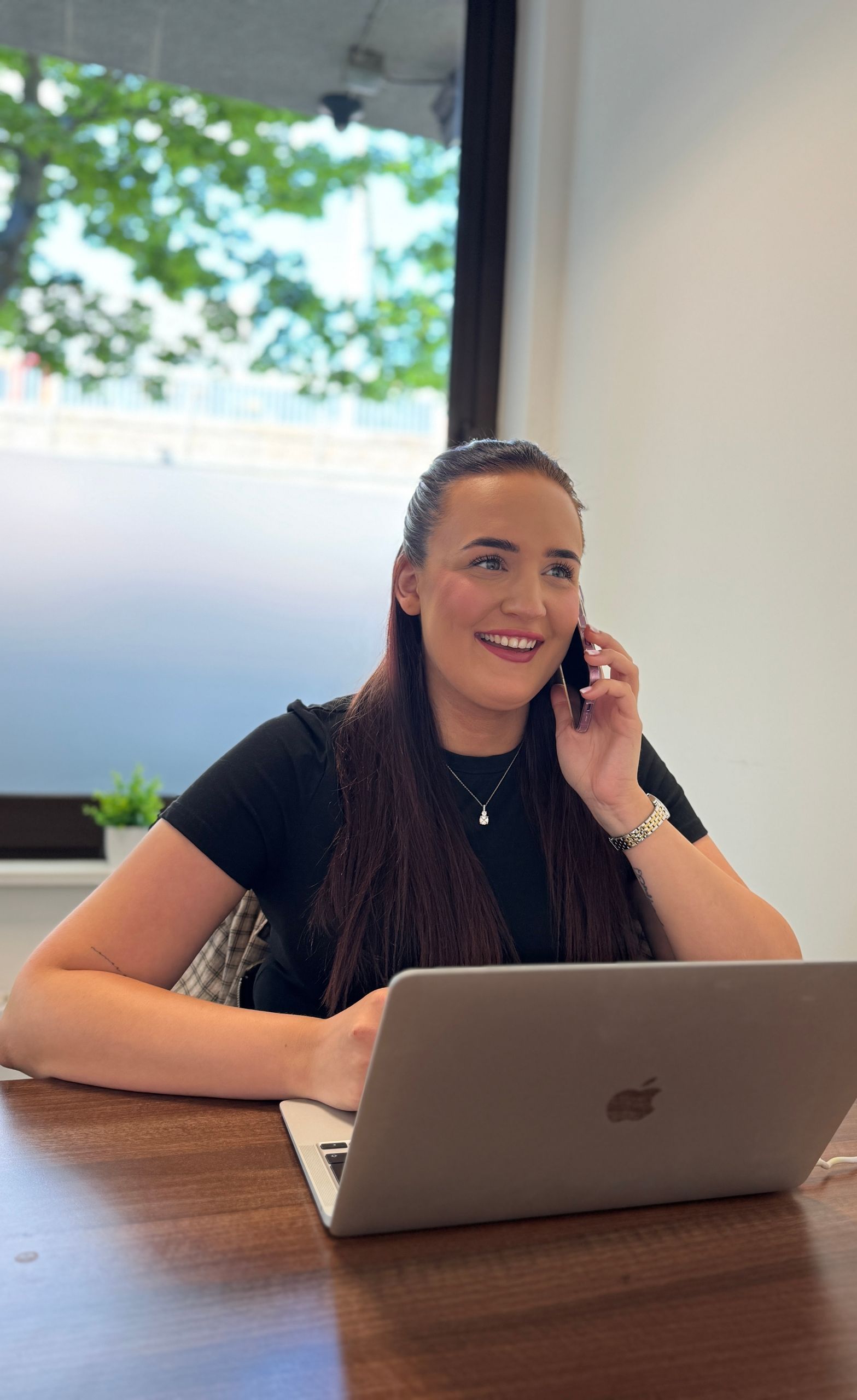 A woman is sitting at a table with a laptop and talking on a cell phone.