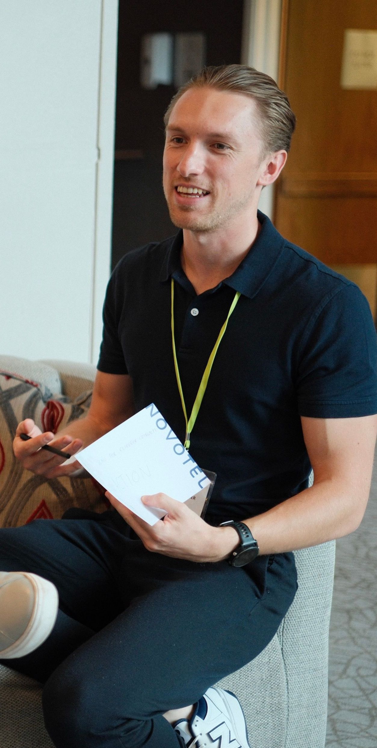 A man in a black shirt is sitting on a couch holding a notebook.
