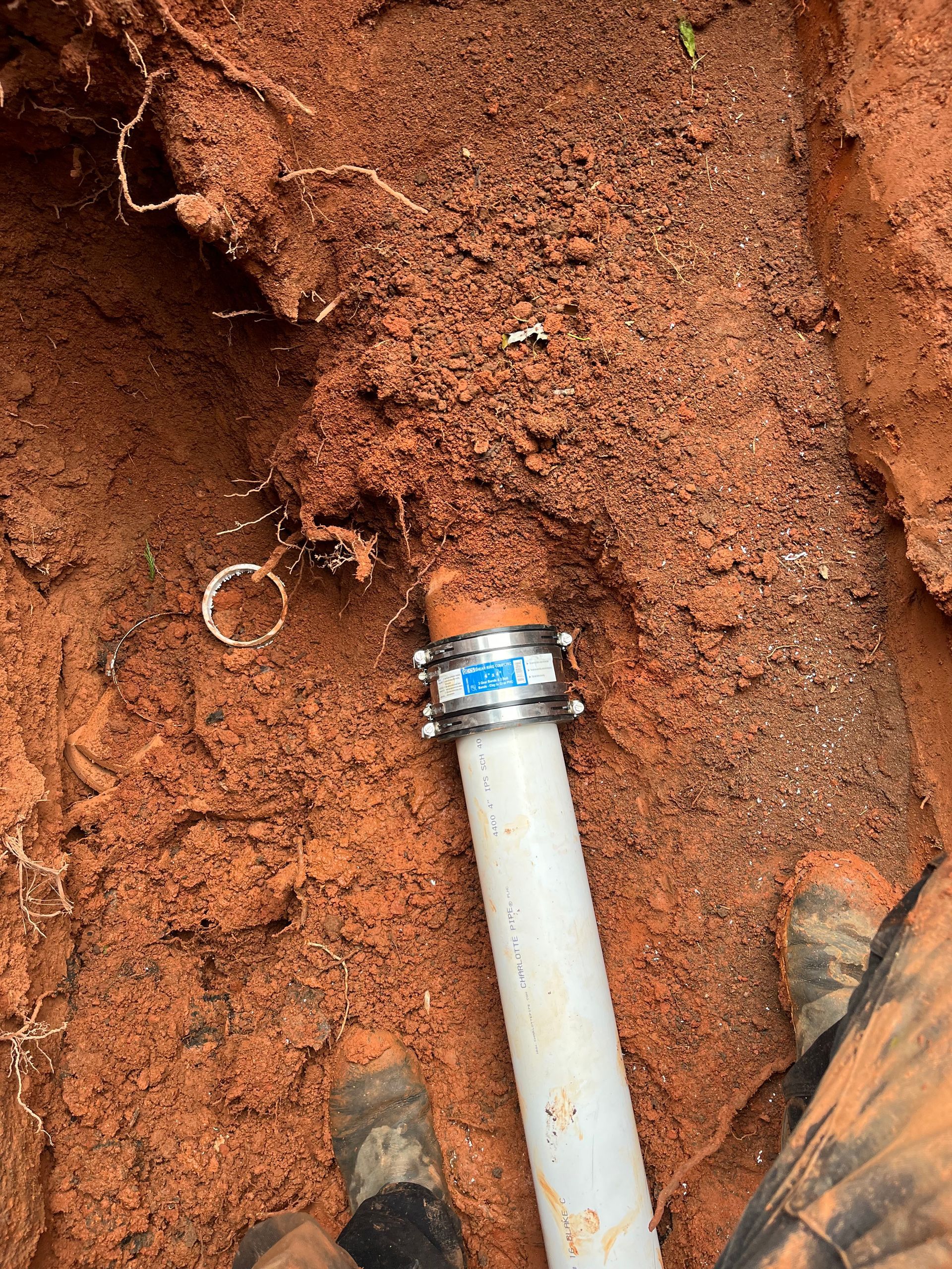 A white pipe is laying in the dirt next to a person 's feet.