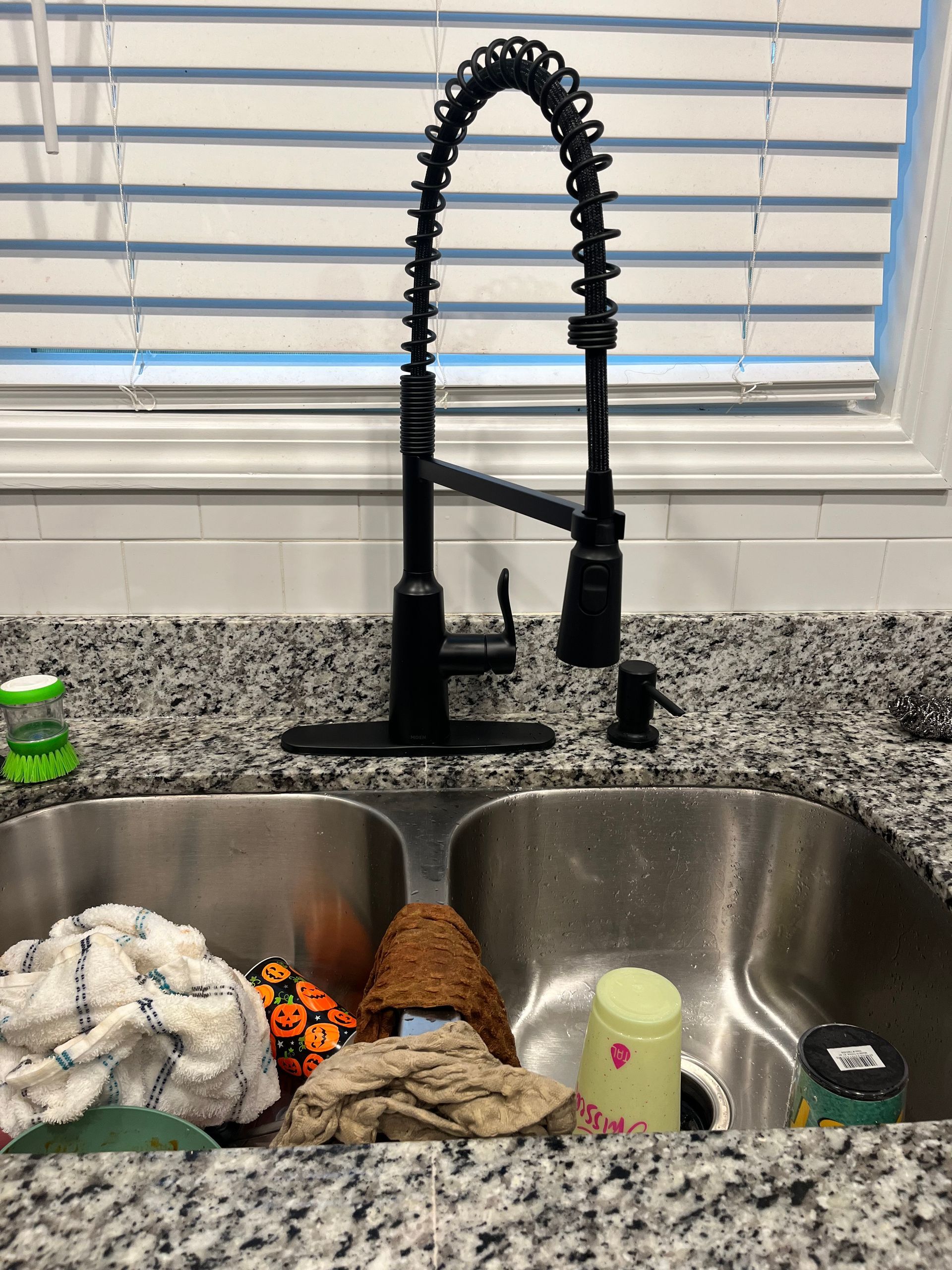 A kitchen sink with a black faucet and a window in the background.